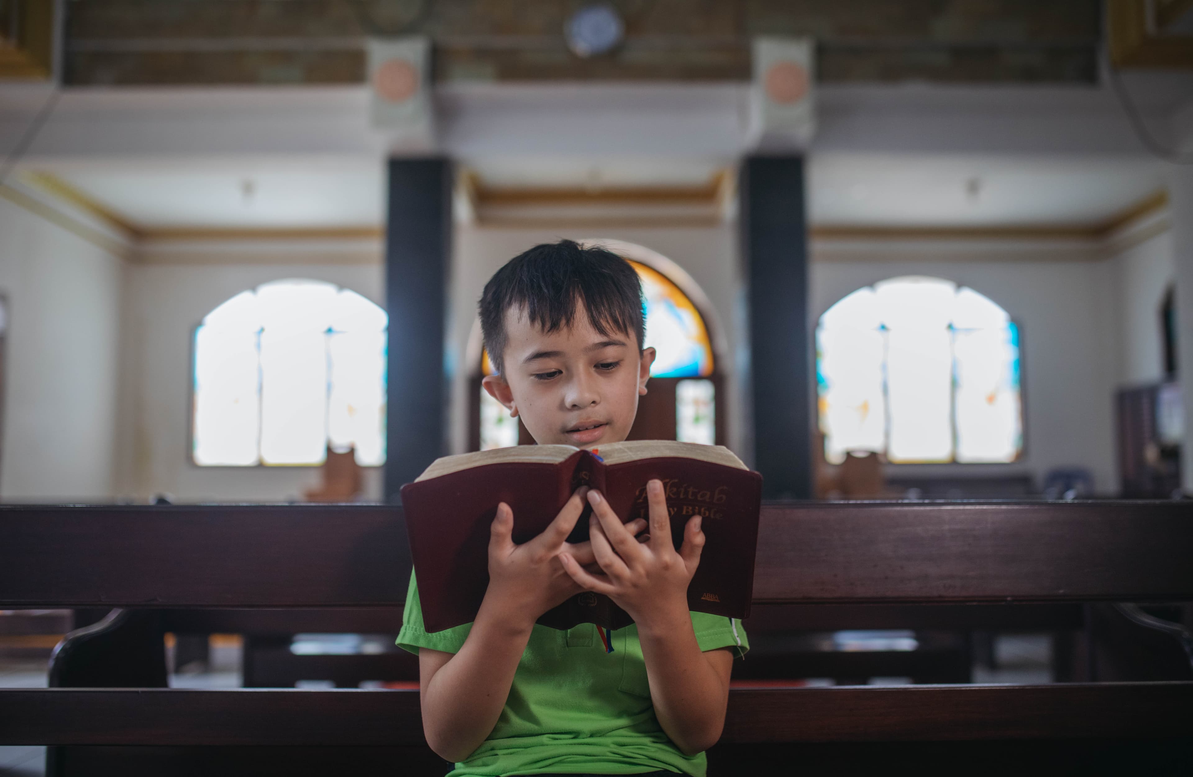 A young boy is reading a bible while holding it close to his face.