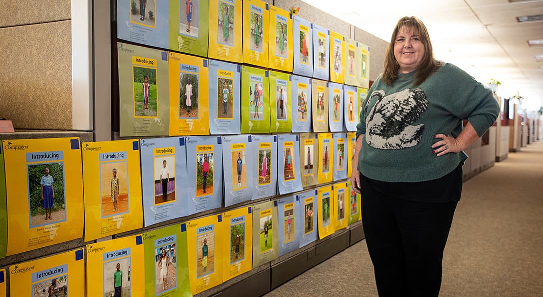 A woman stands next to a wall of sponsored child photos.