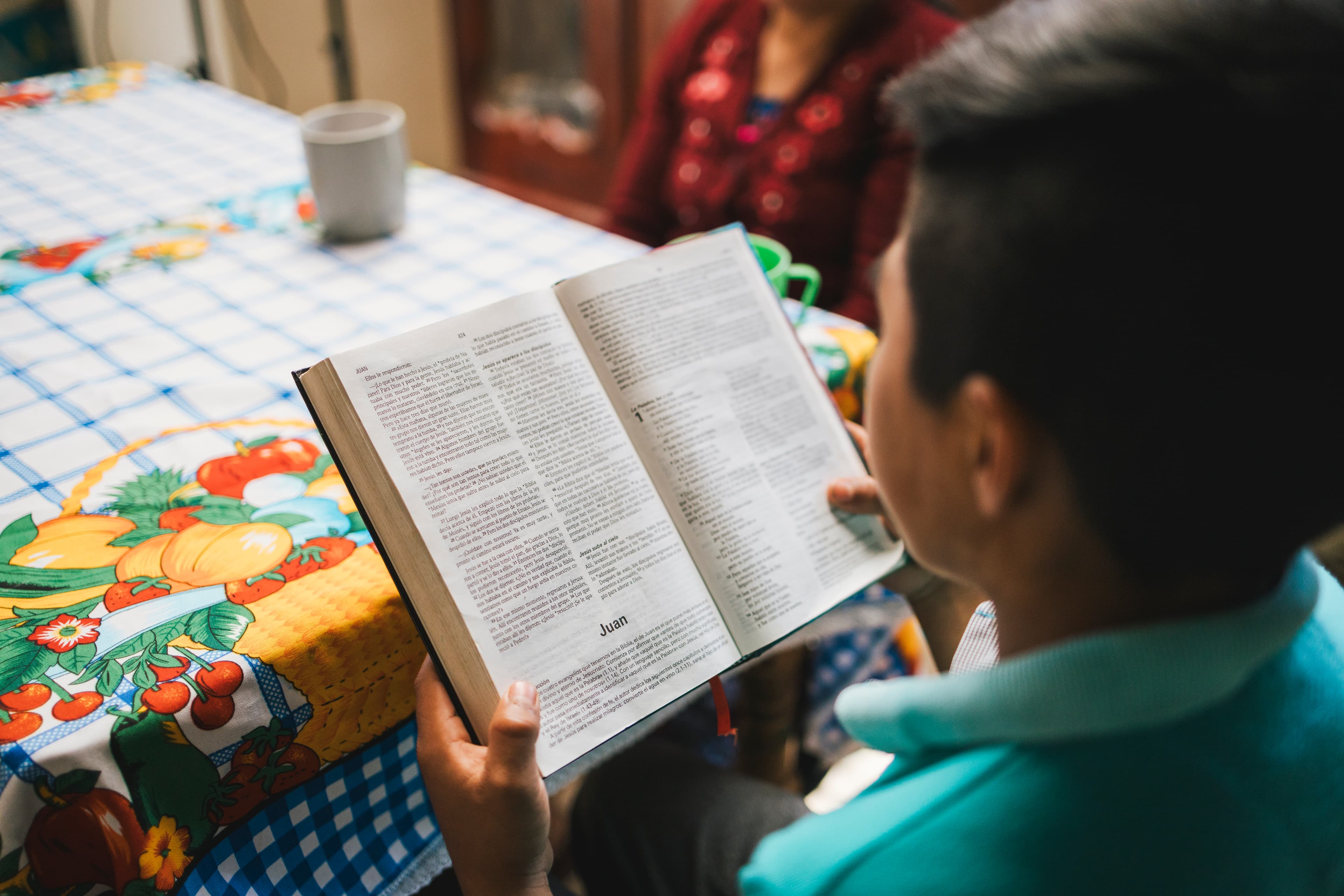 A young boy sits at a table while reading an open Bible.