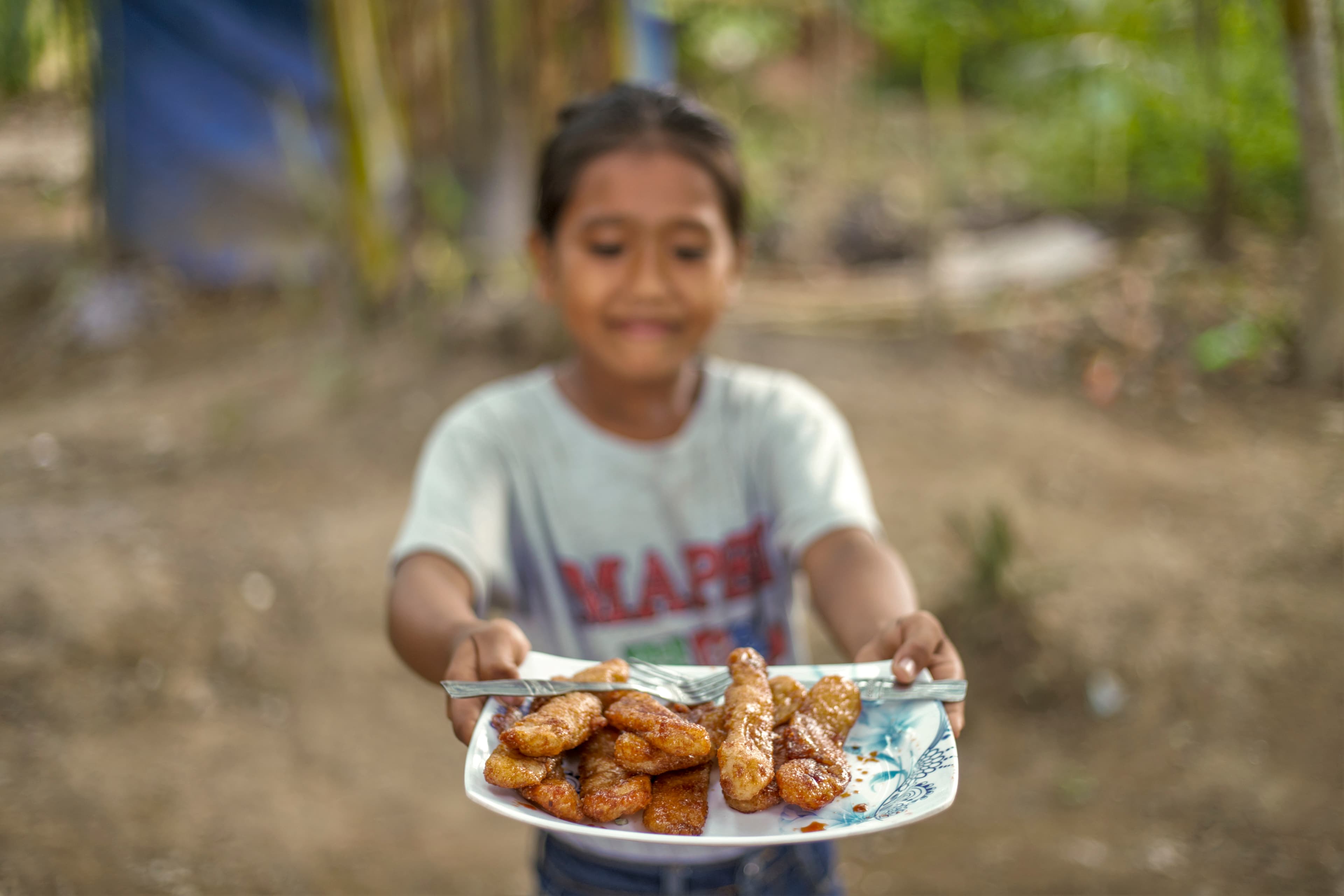 A young girl is holding up a plate with food to share.