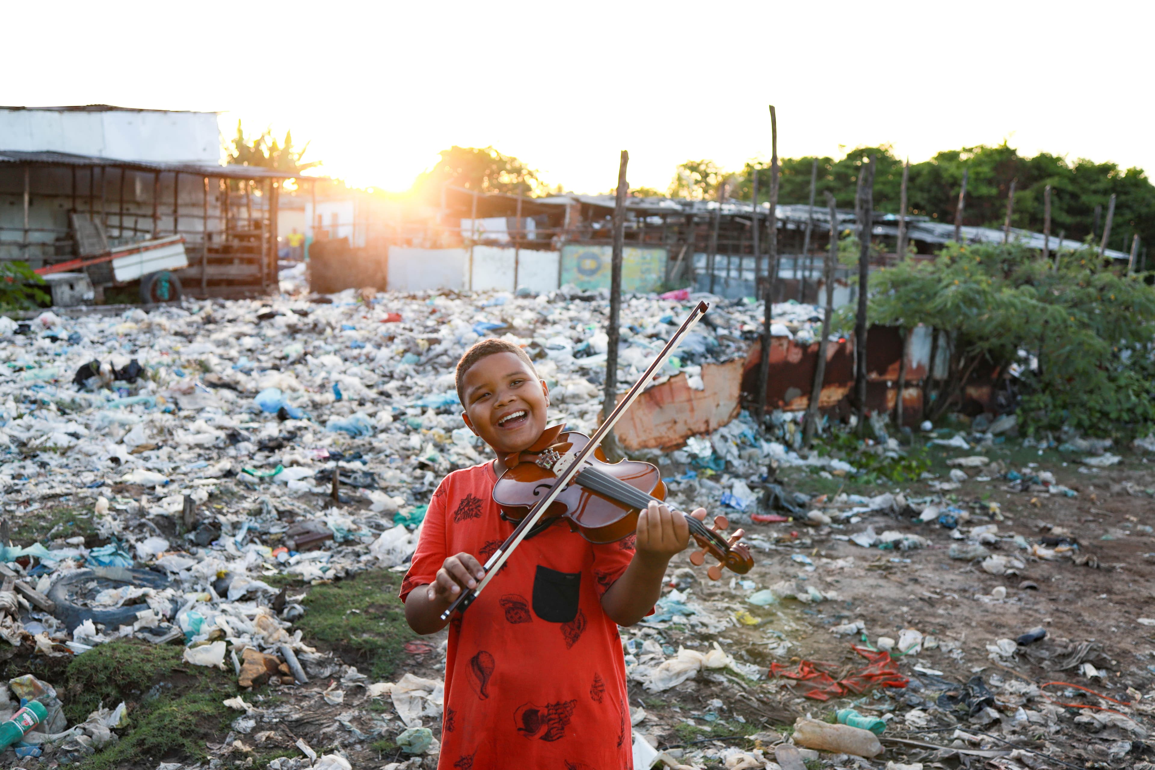 A young boy wearing a red shirt plays the violin while smiling widely.