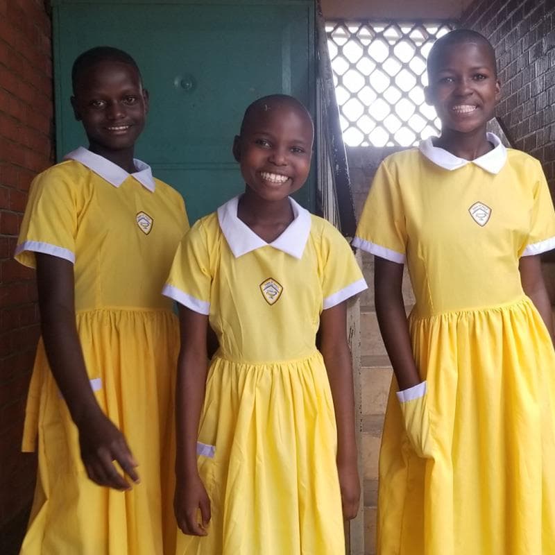 Three young African girls wearing yellow dresses smile for the camera.
