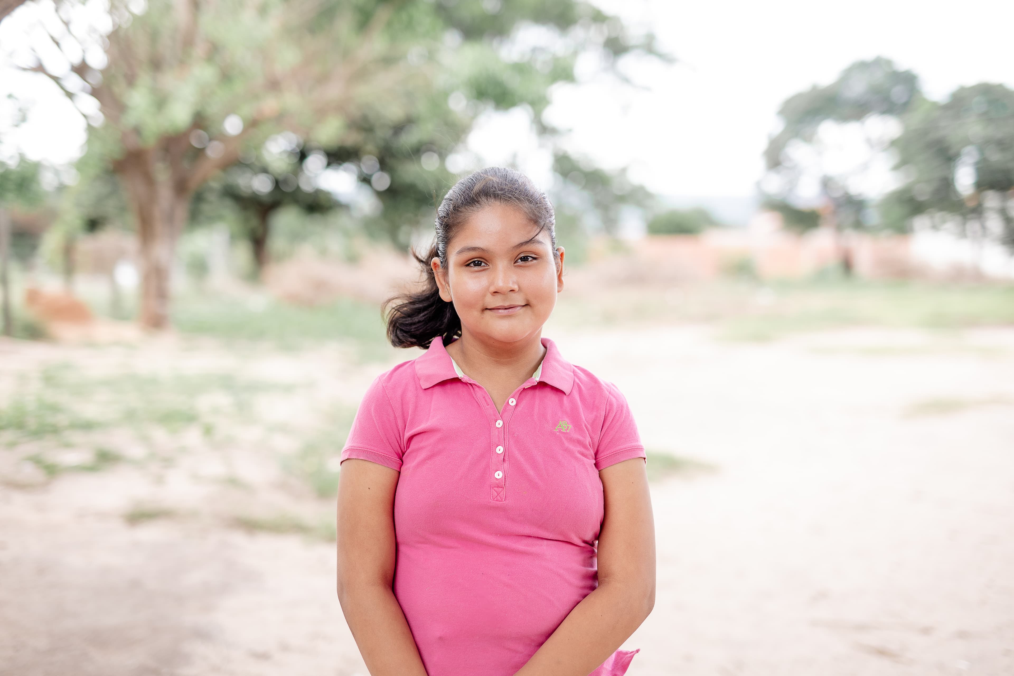 A teen girl wearing a pink shirt smiles for the camera.