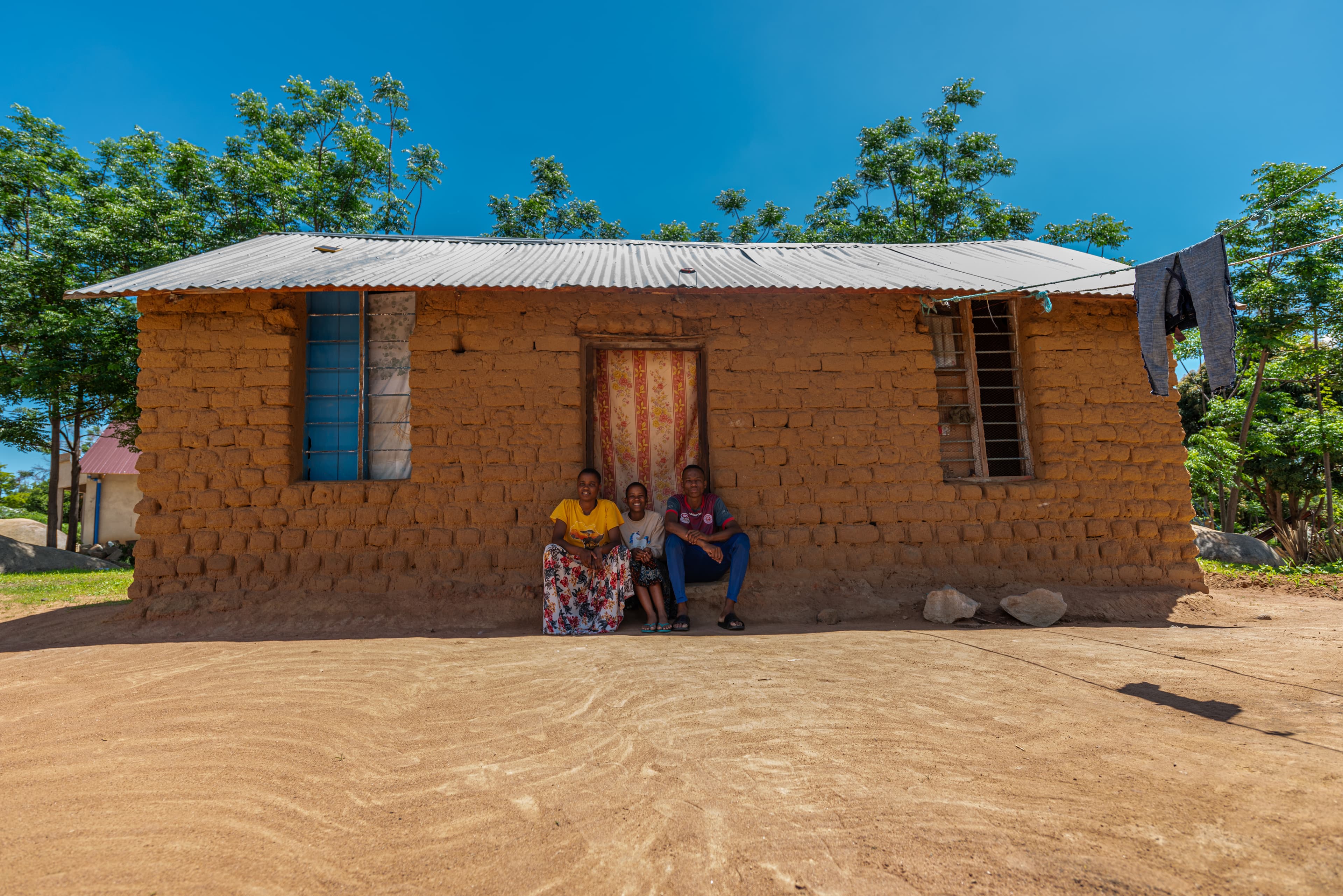 A teenaged girl sits between her older sister and brother on the steps of their home in Tanzania.