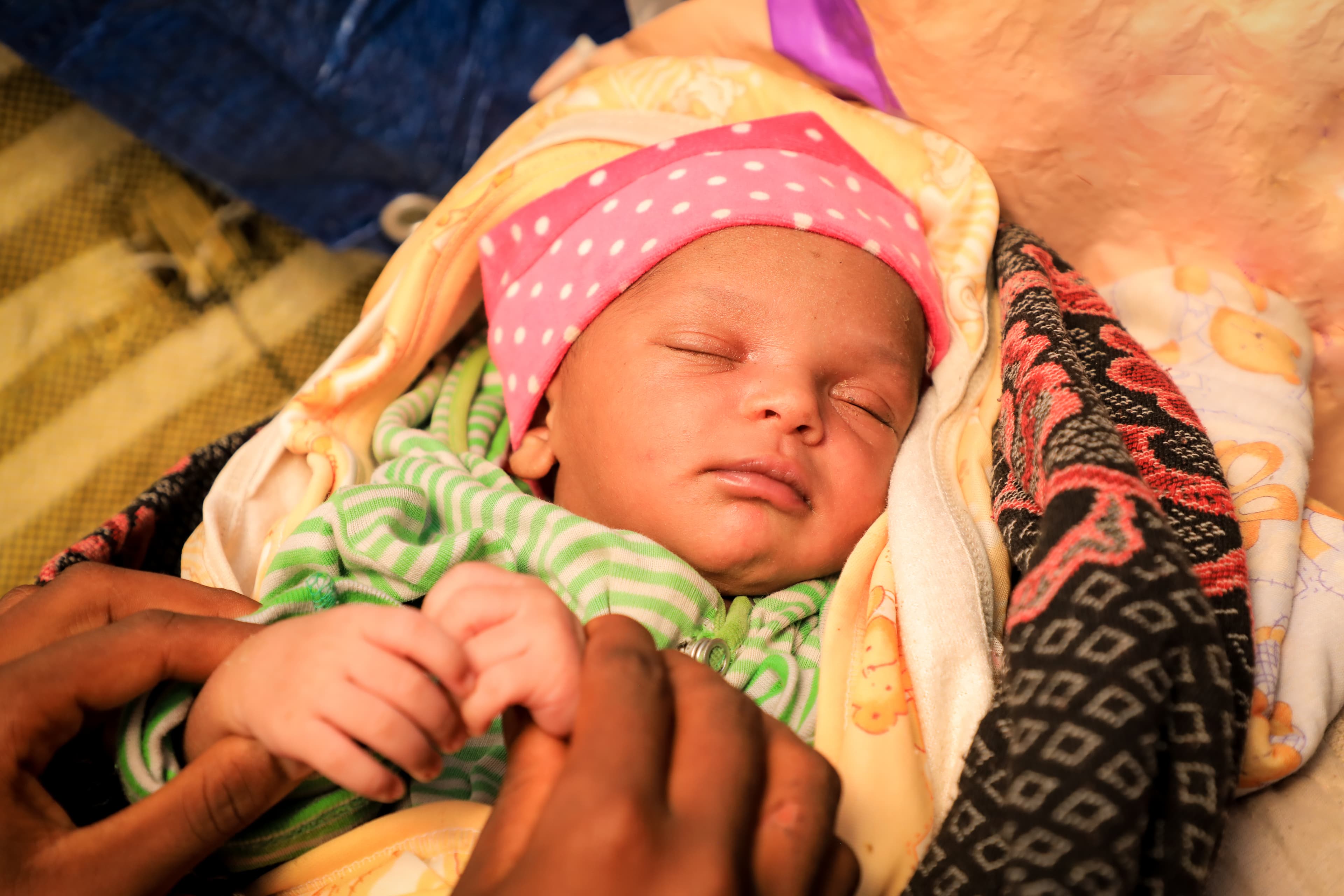 A newborn baby girl sleeps soundly inside brightly colored shawls.