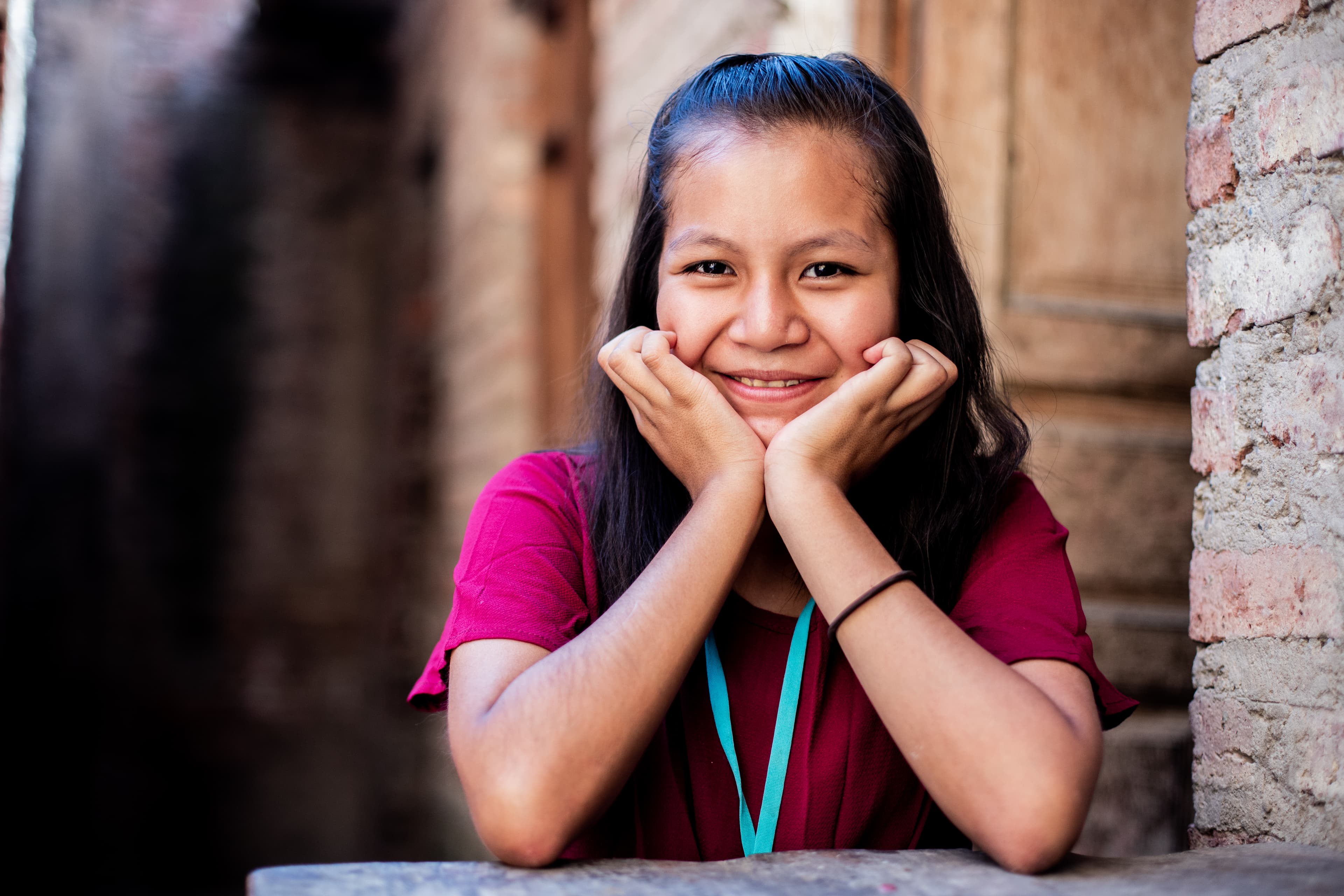 A young girl is resting her face in her hands with a smile on her face.