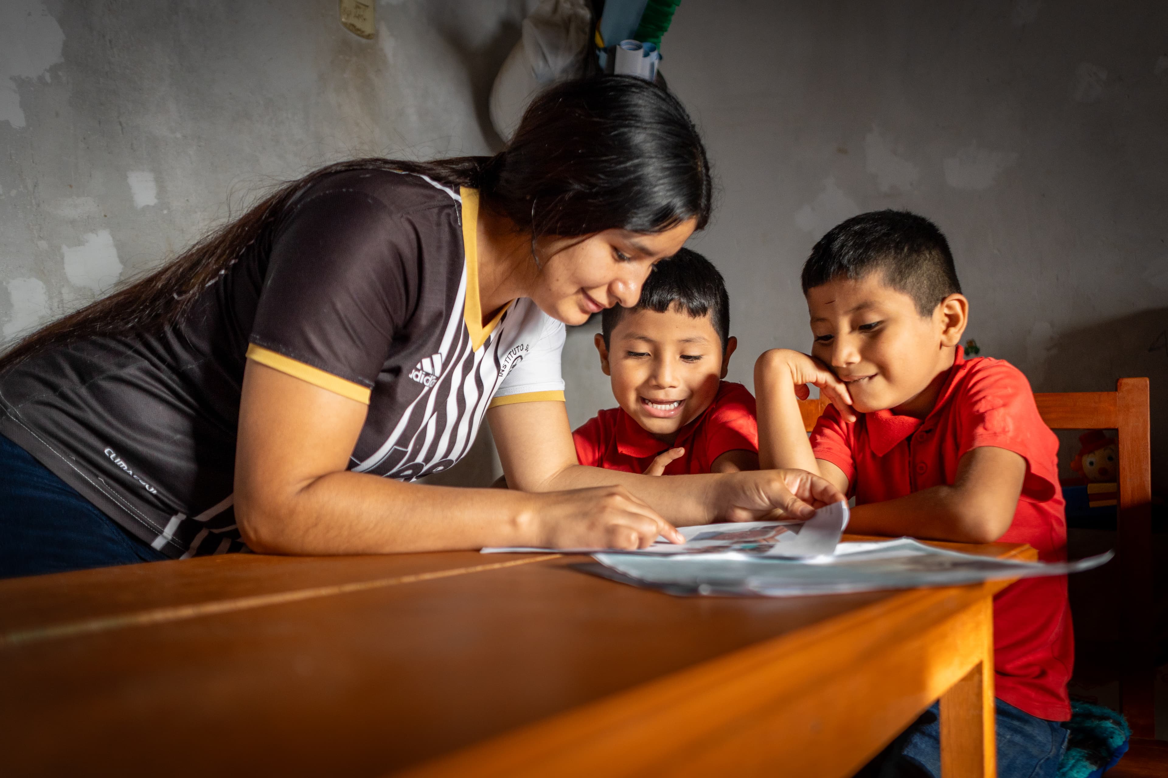 Two young boys and a Compassion center staff member smile as they read a letter from the boys’ sponsor.