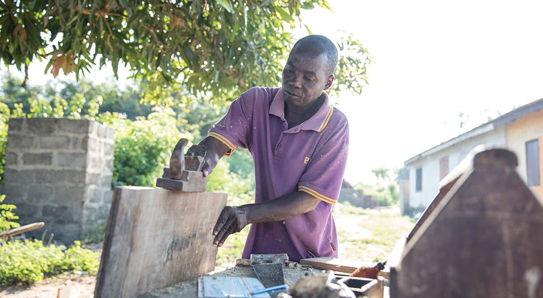 An older man works to smooth out a wooden board with a sander.