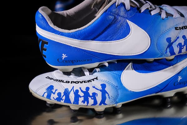 Blue and white football cleats featuring "End Child Poverty" and an image of children.