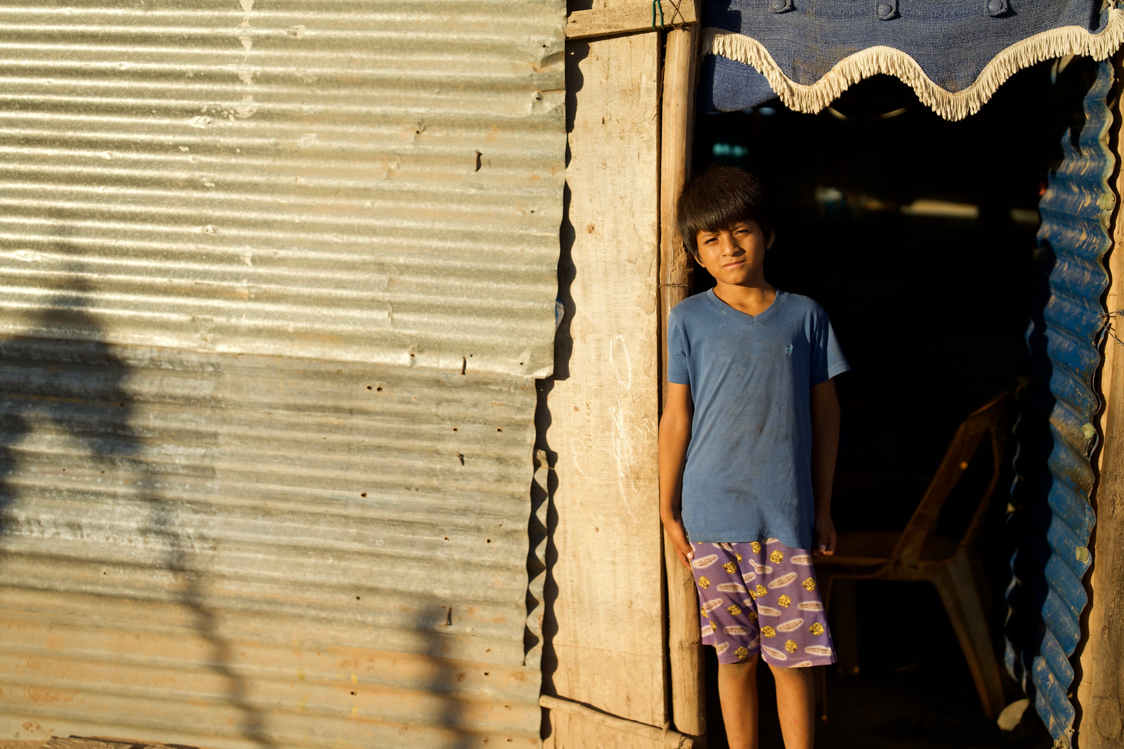 A boy is standing in front of his home looking at the camera.