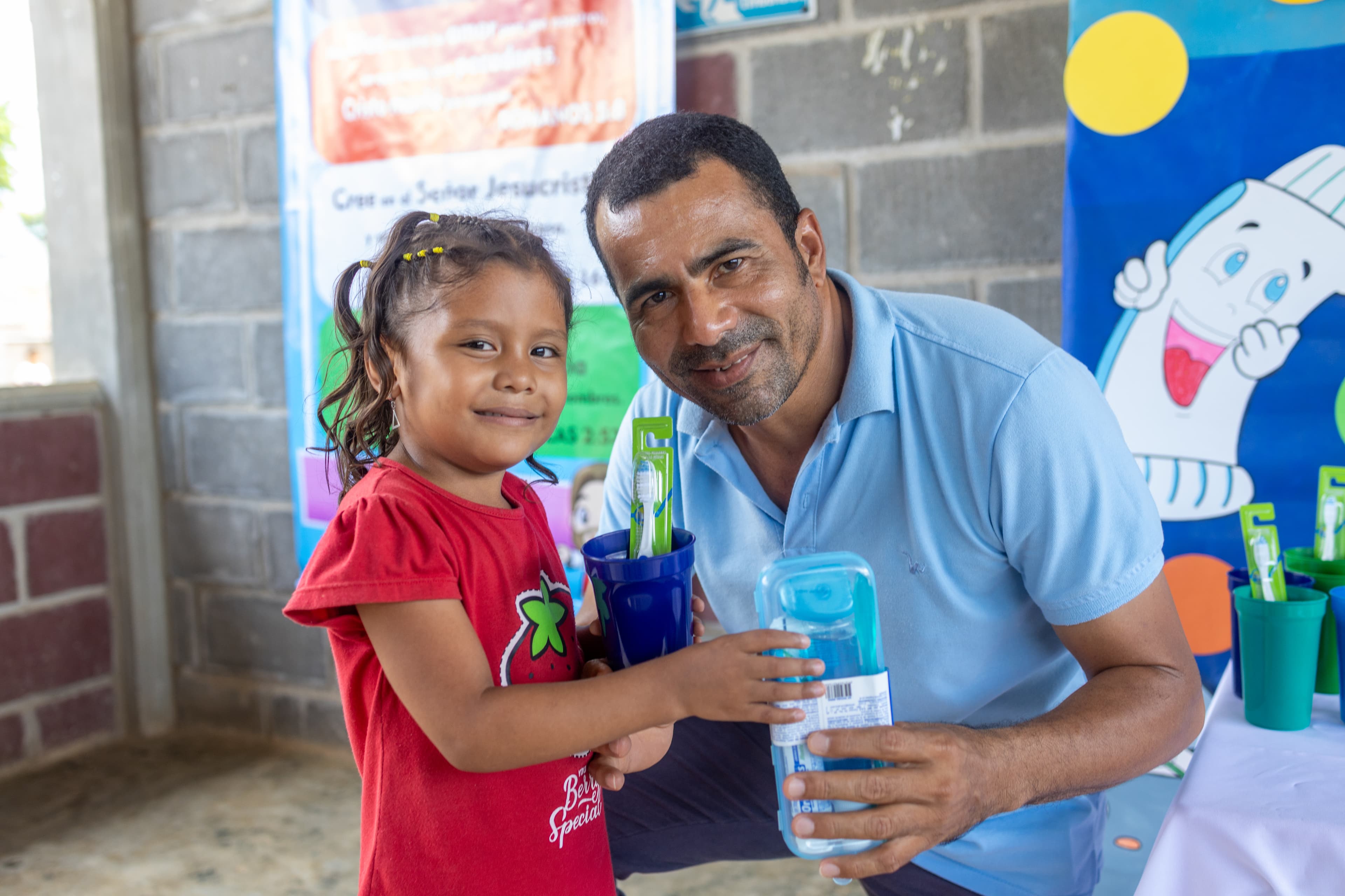 Little girl smiles standing with her pastor who is distributing toothbrushes and dental kits.