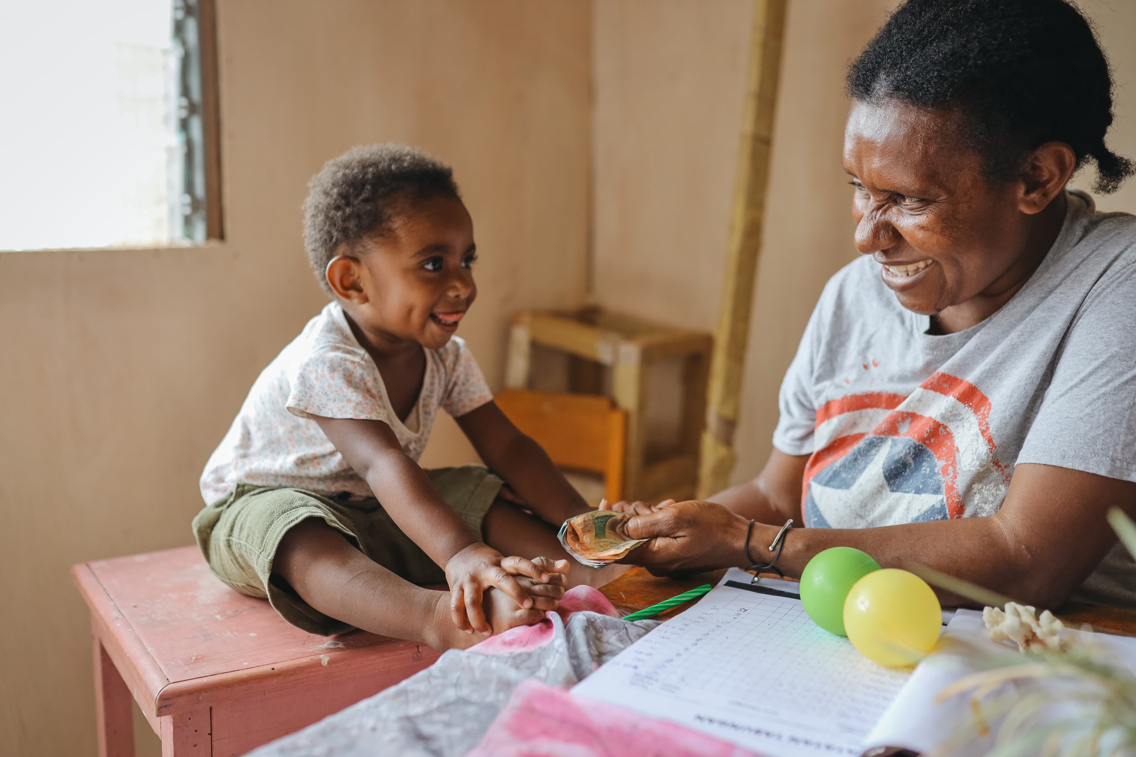 A baby is sitting on a small table with her mother in a classroom at the Compassion Center.