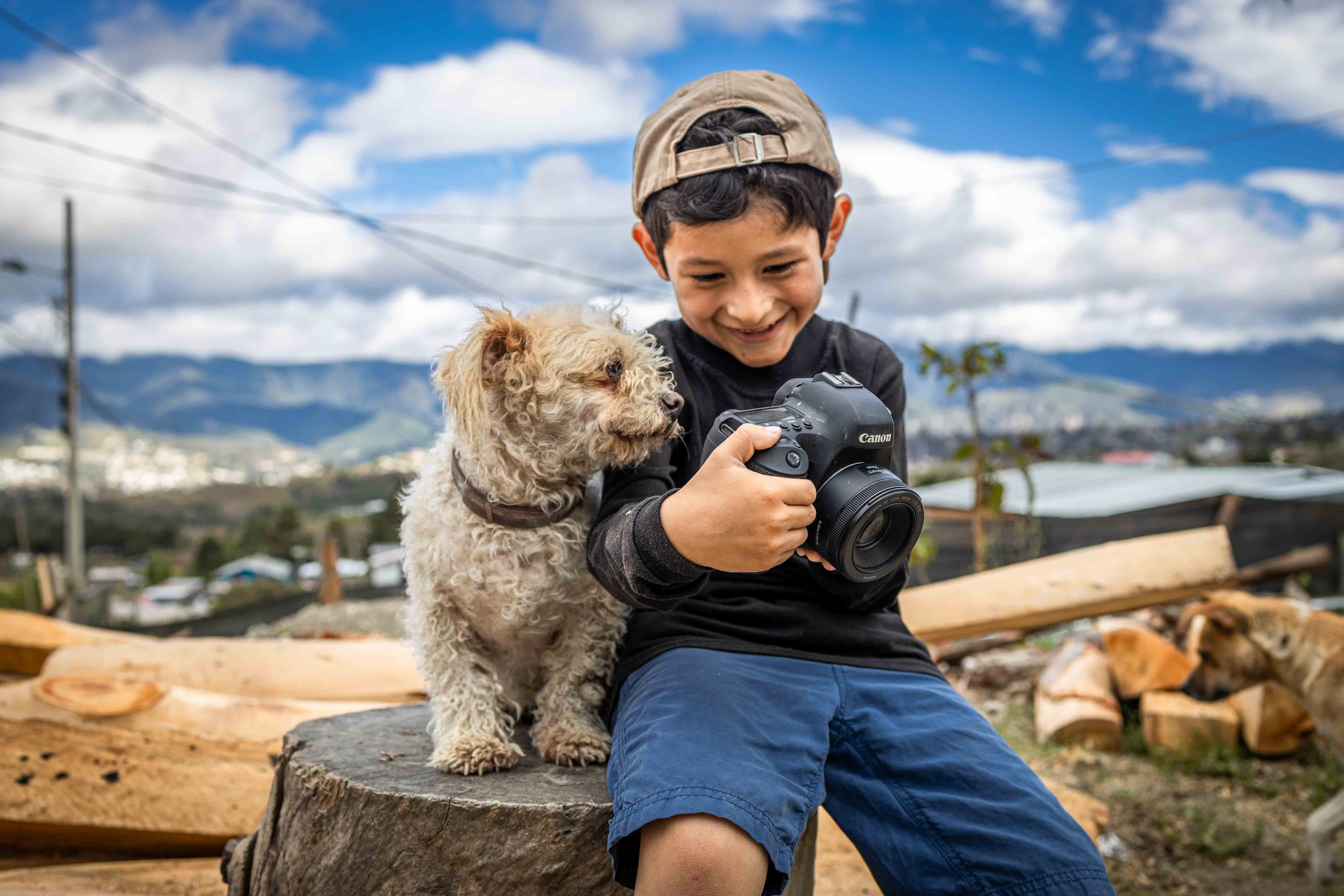 A young boy shows a camera to a dog while smiling.