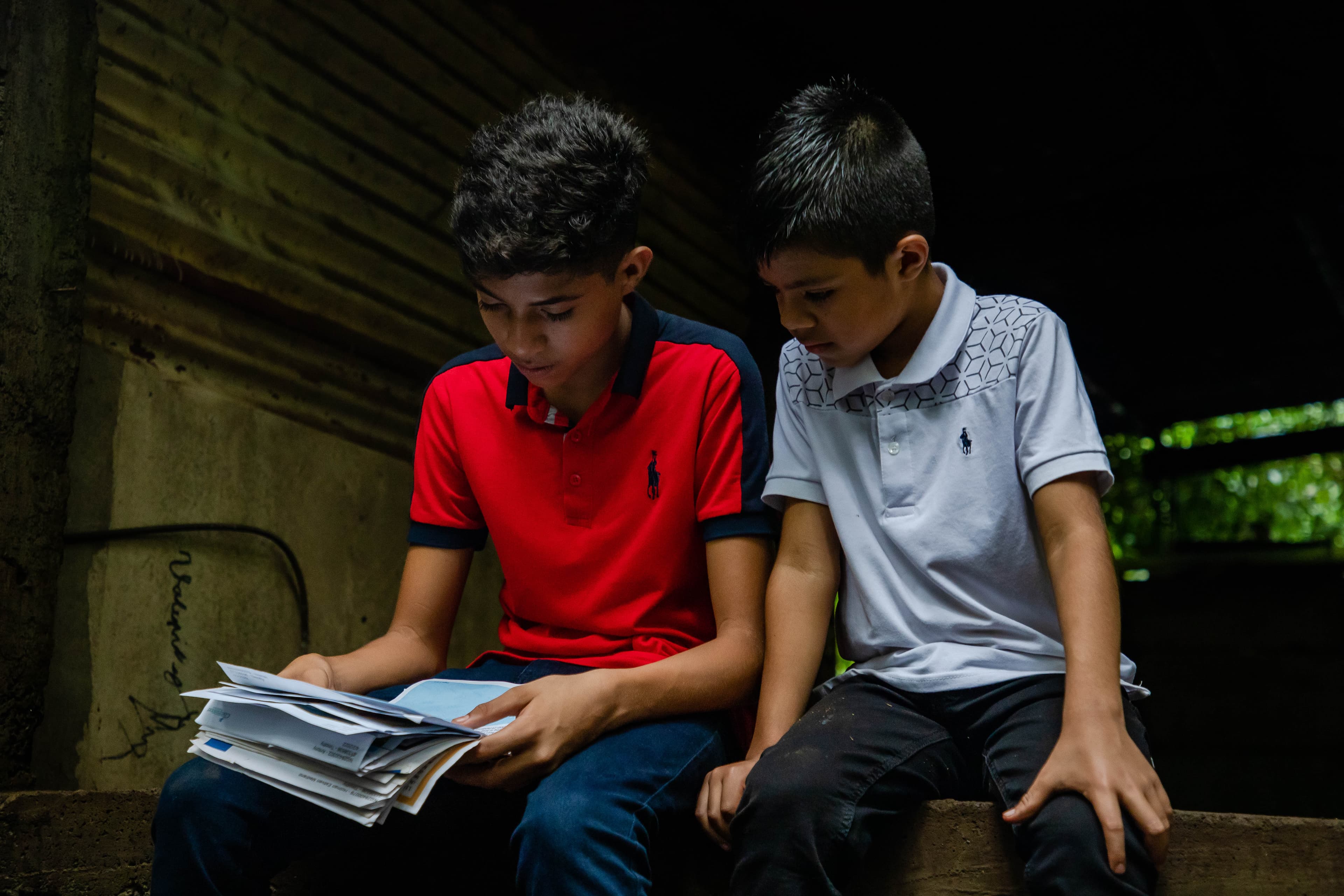 Two young boys are sitting and reading letters from their sponsors together.