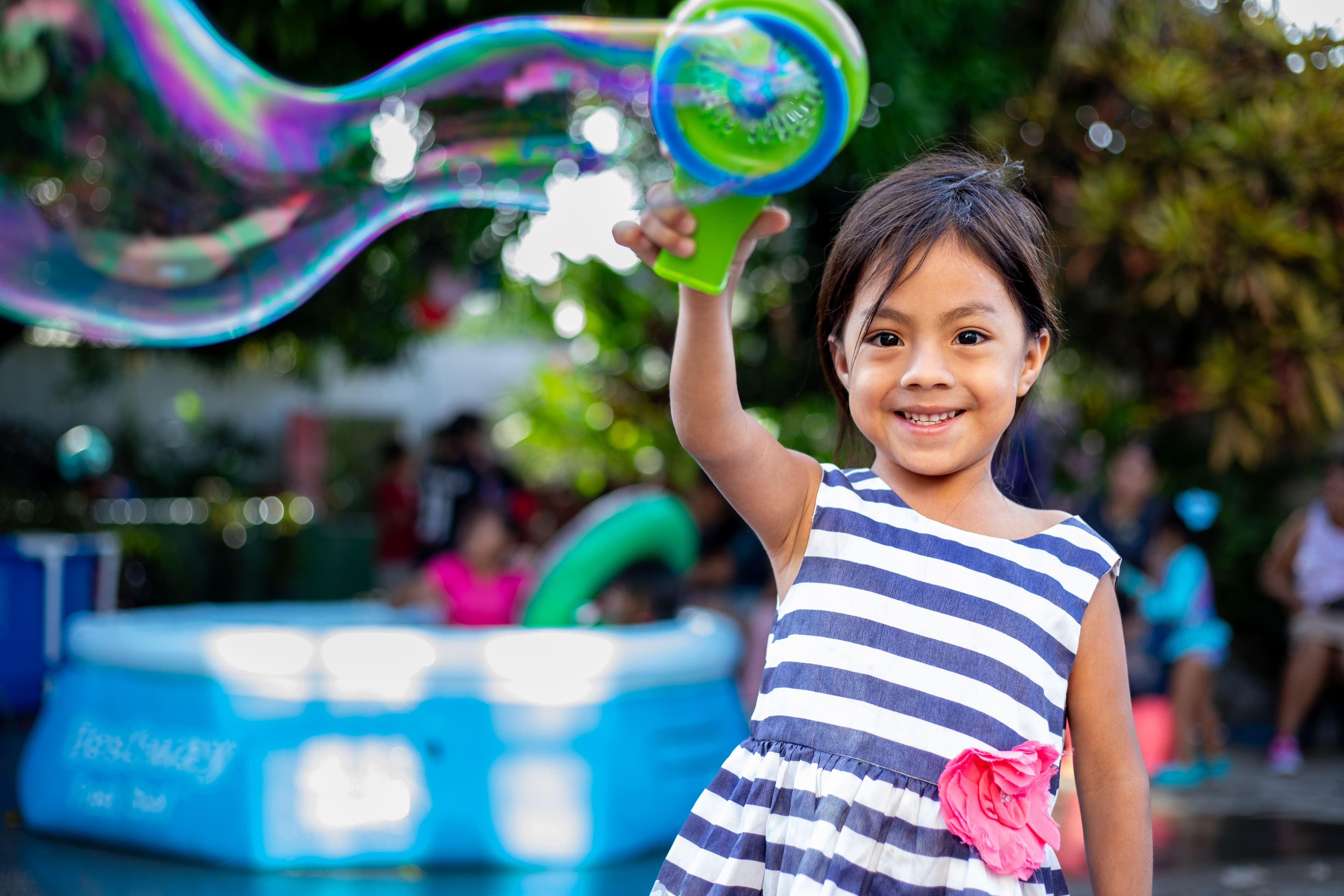 A young girl is smiling as she lifts her hand in the air playing with bubbles.