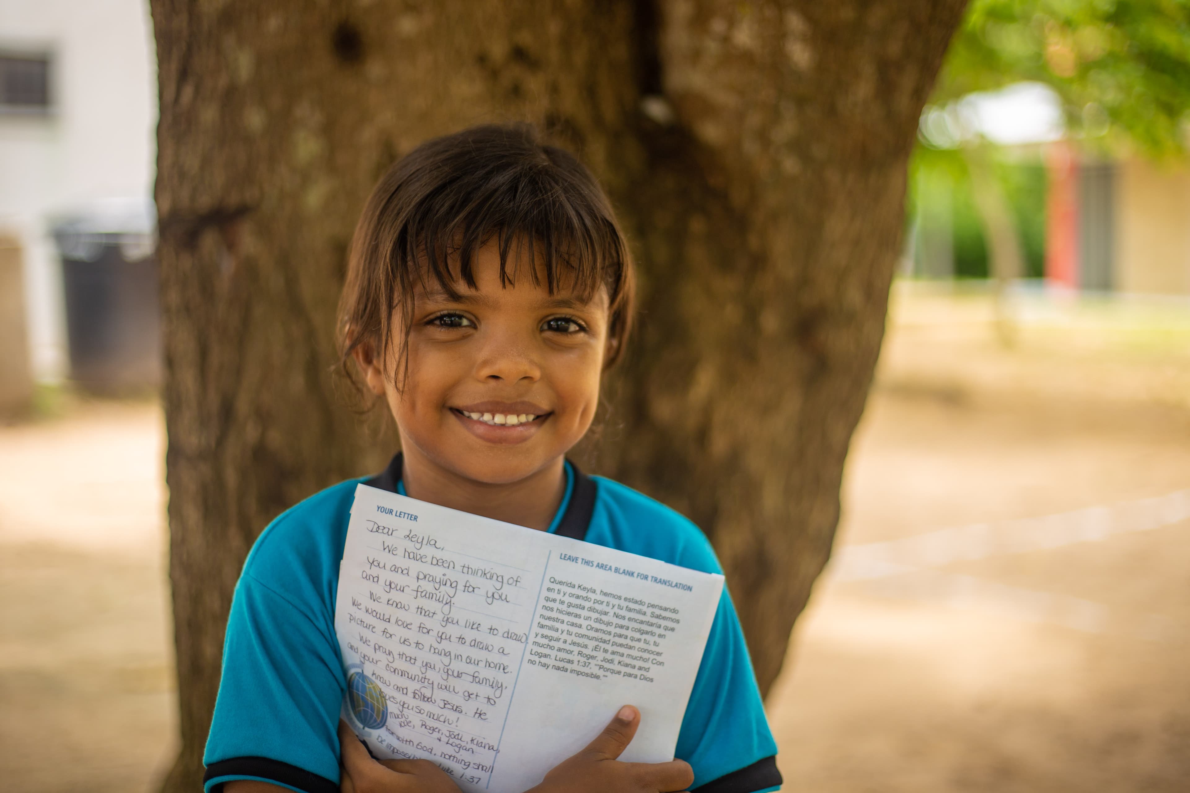 A young girl is smiling as she holds a sponsor letter