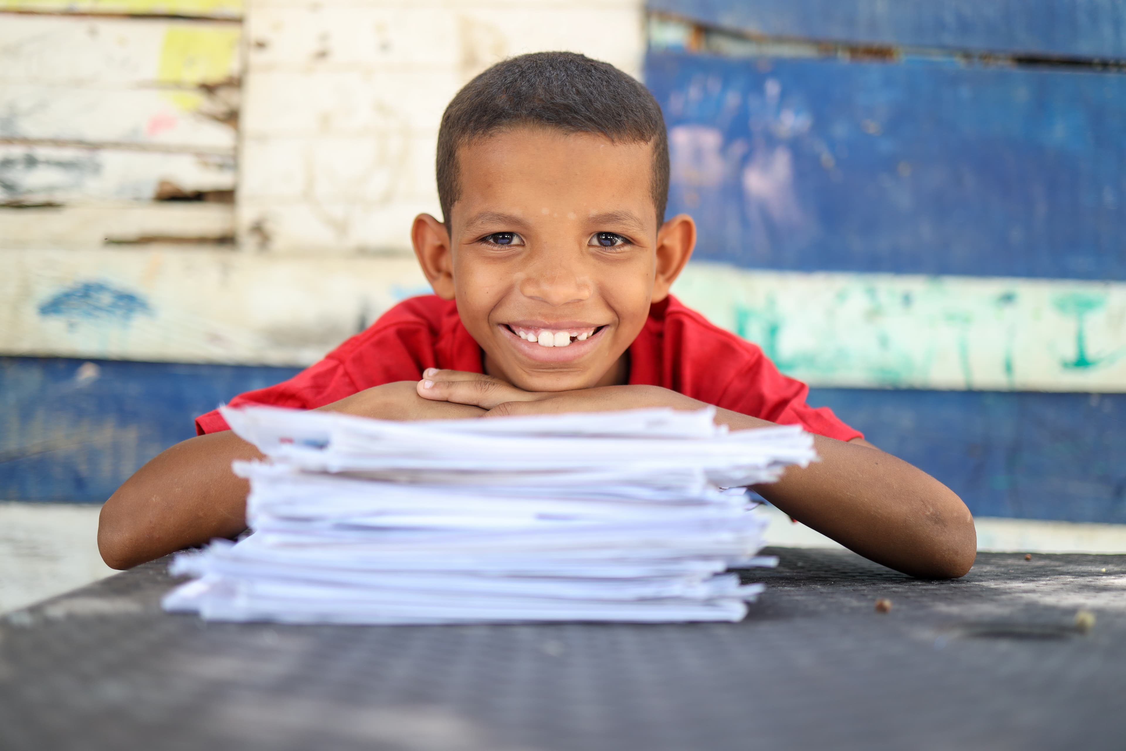 A young boy smiles with his hands and chin resting on top of a stack of letters from his sponsor.