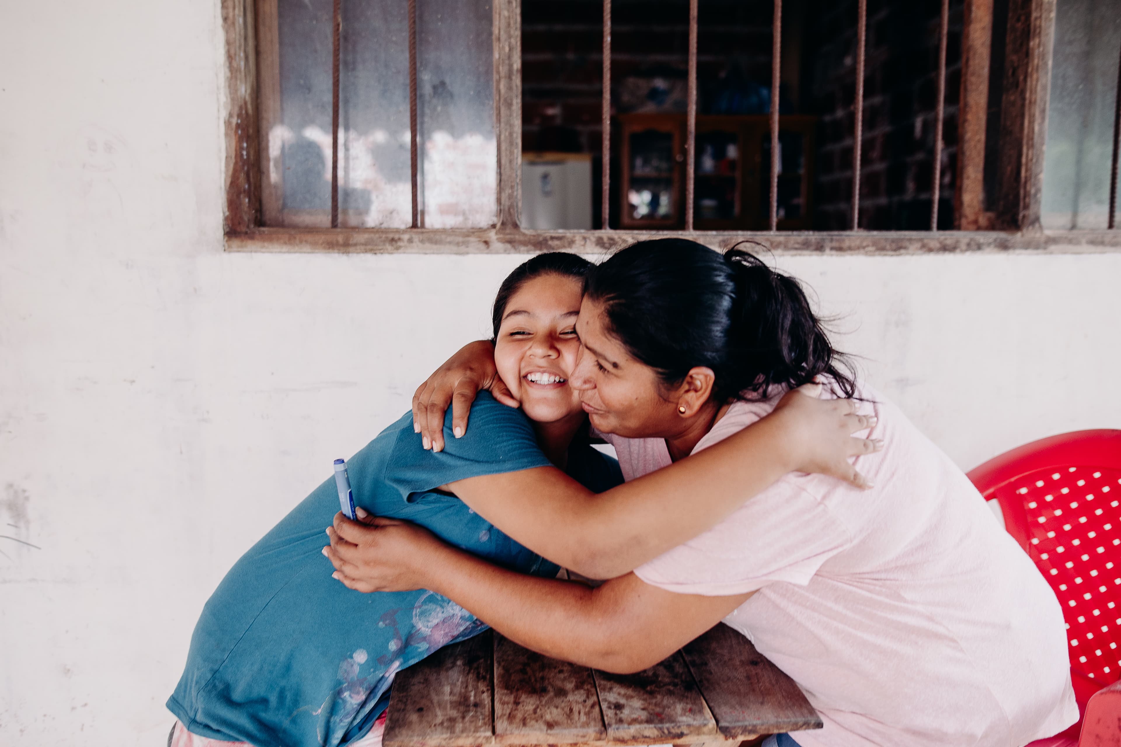 A young girl and her mom embrace over a table.