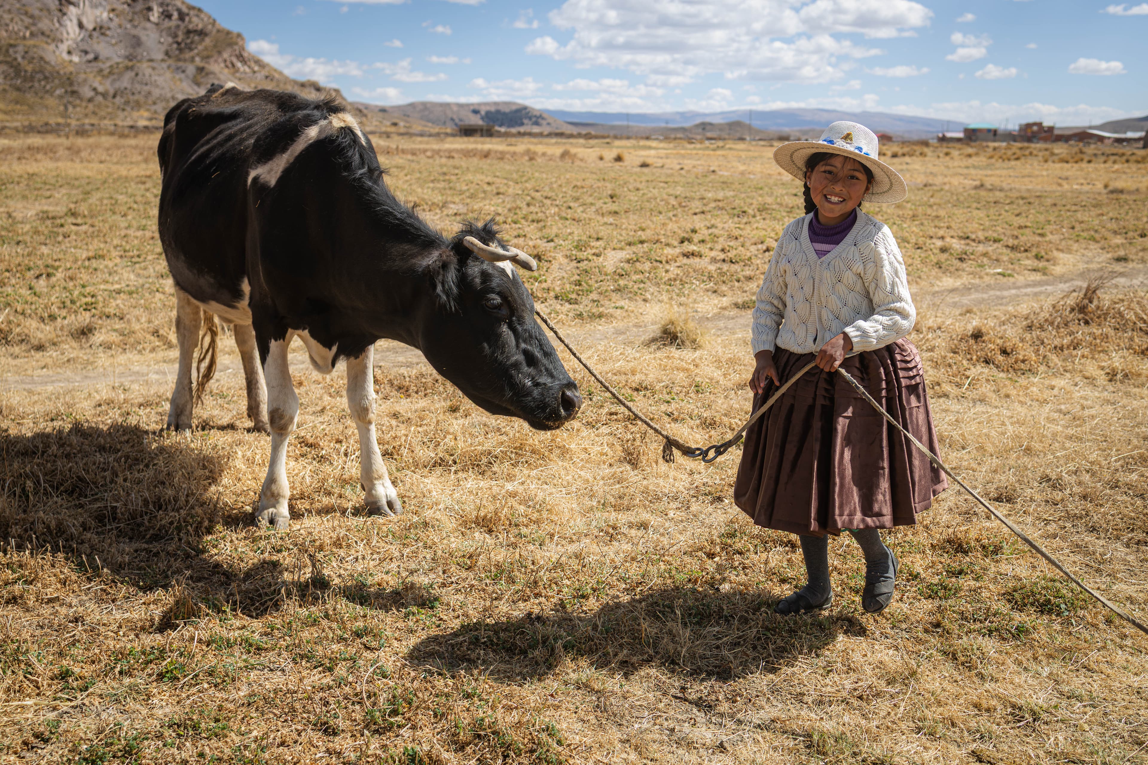 A young Bolivian girl stands next to a cow while smiling.