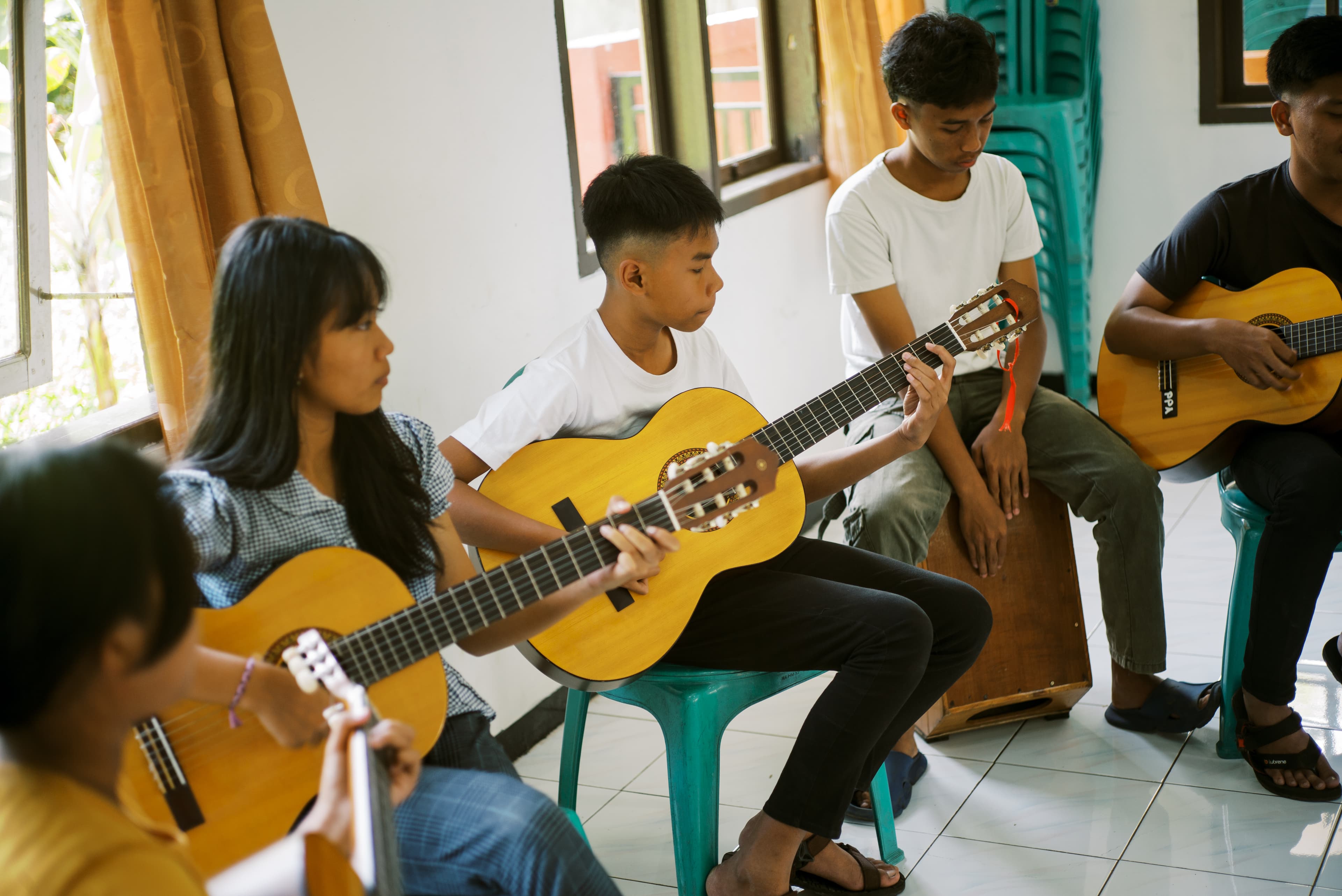 A young adult and his friends from the guitar class are sitting together practicing.