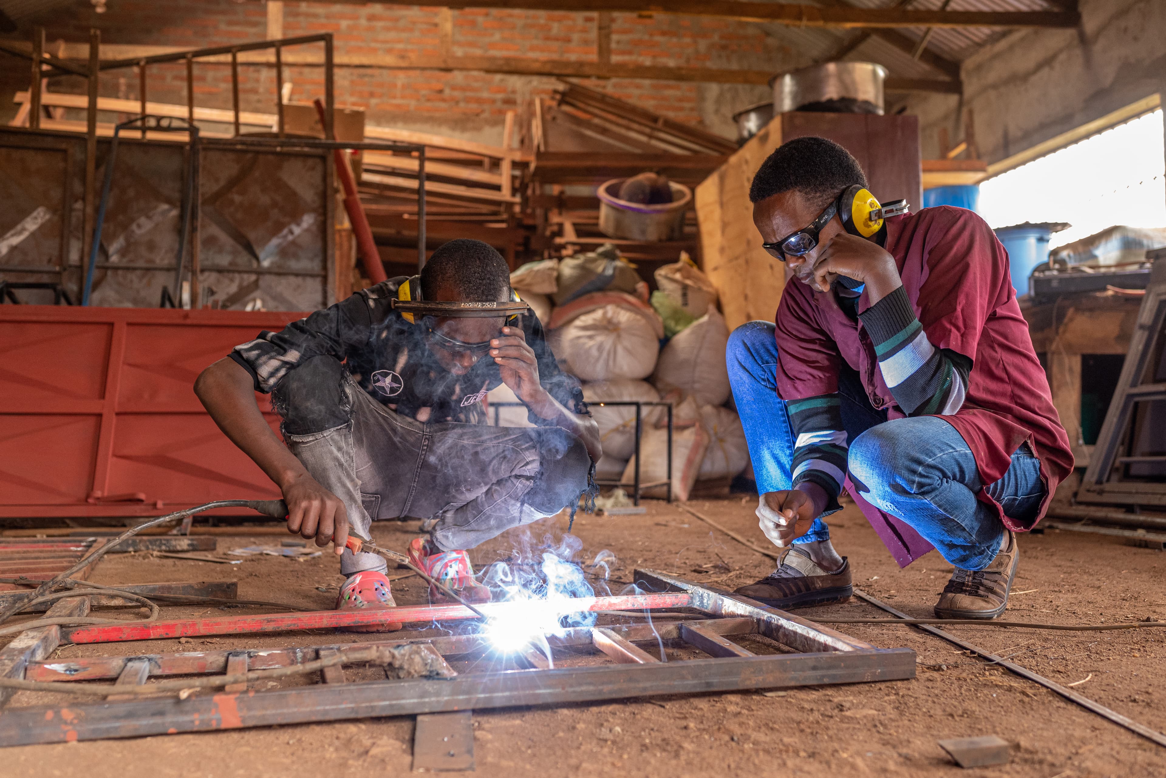 Two young men are wearing protective eye gear and kneeling down in the Compassion workshop.