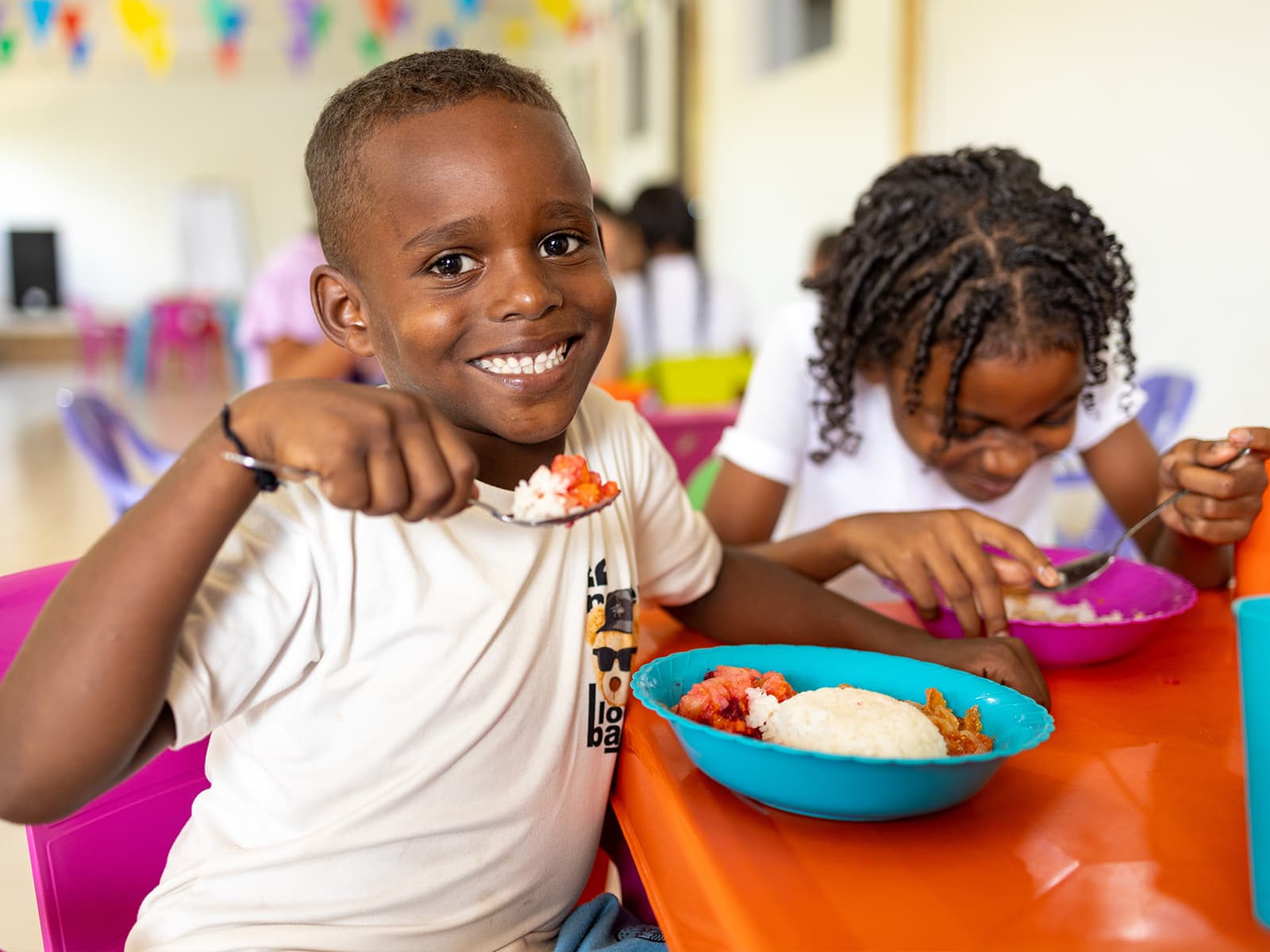 A young boy smiles as he holds a spoon of food