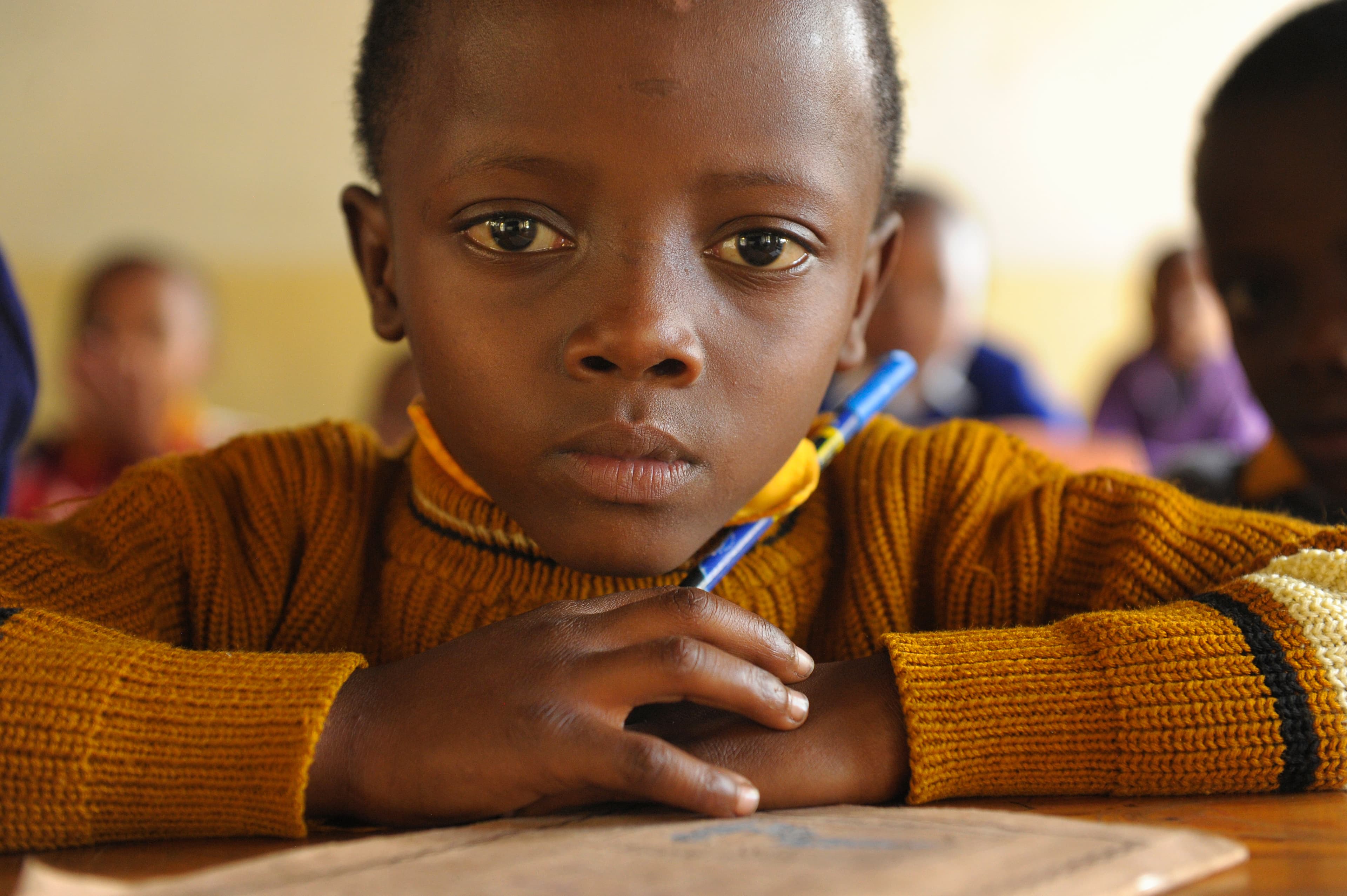 A young child is sitting at a desk looking at the camera.