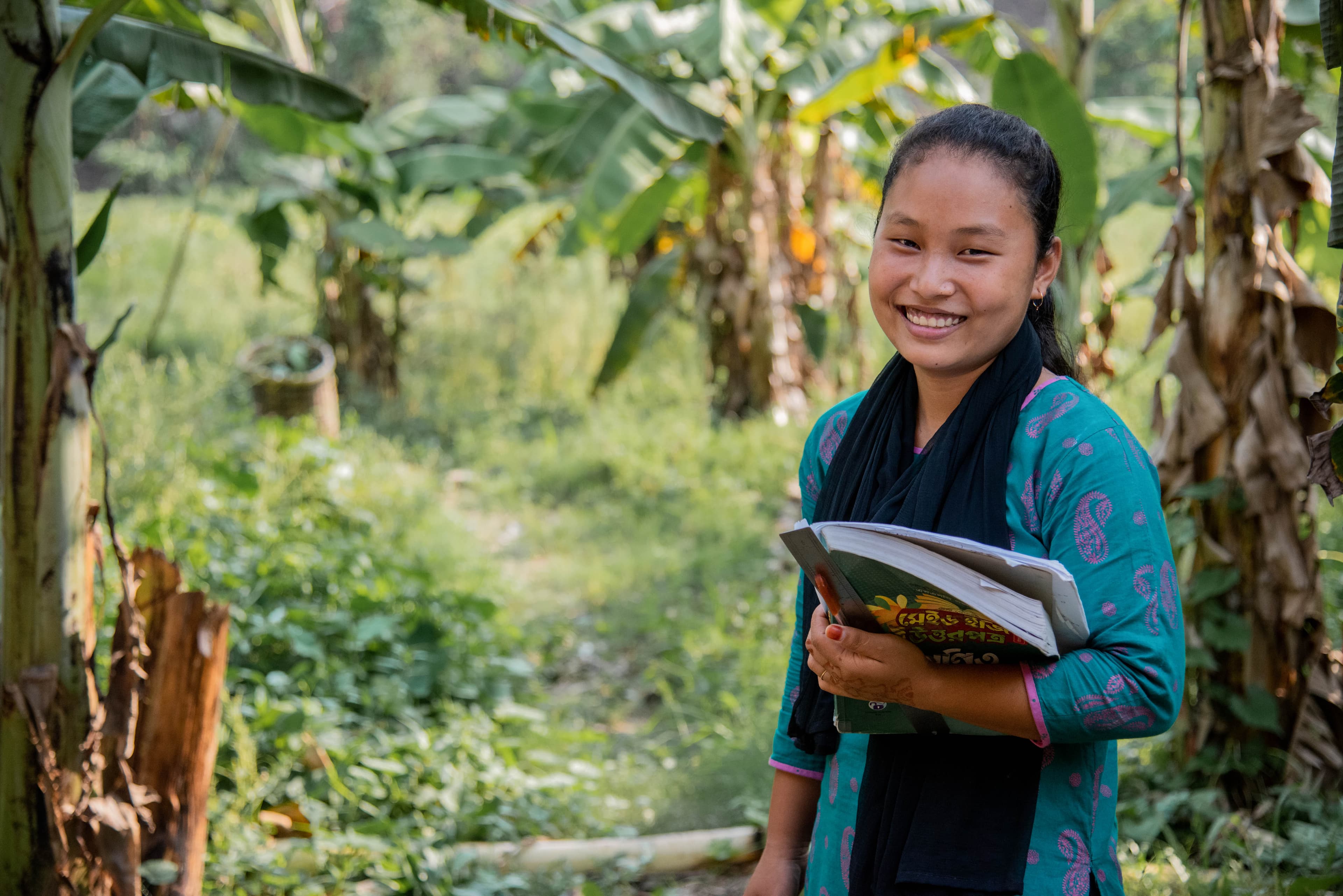 Shanti is standing in the pathway by her school holding her books.