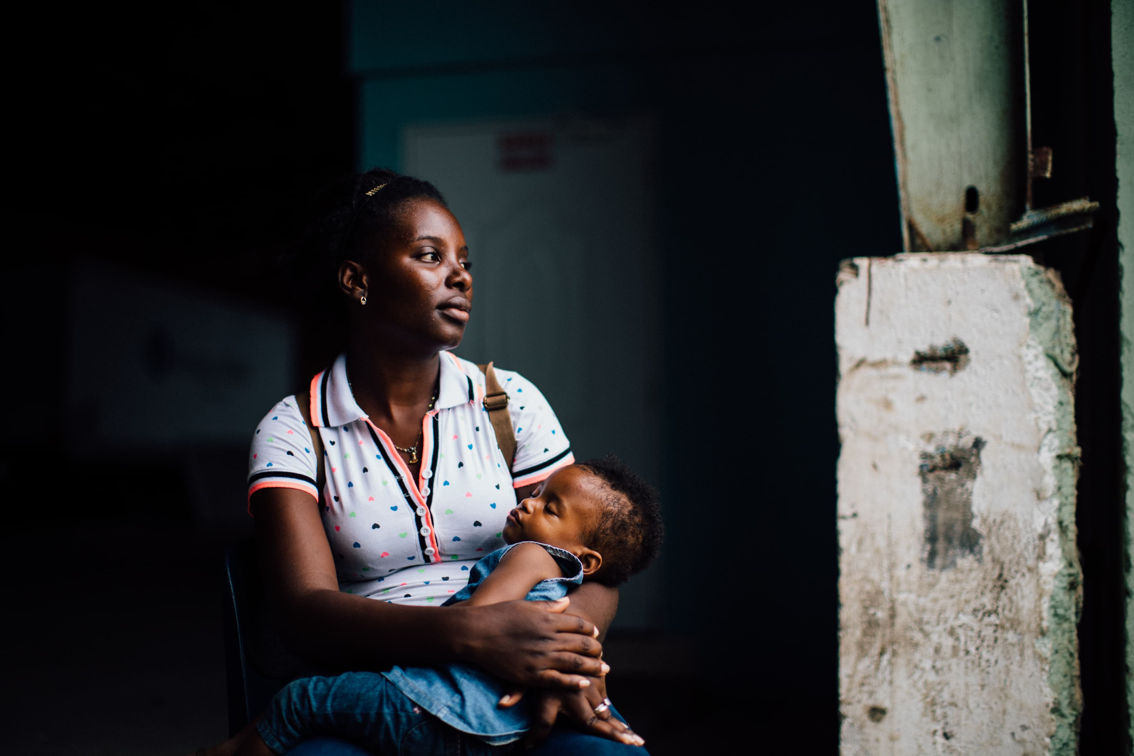 A mother is sitting as she holds her sleeping baby in her arms.