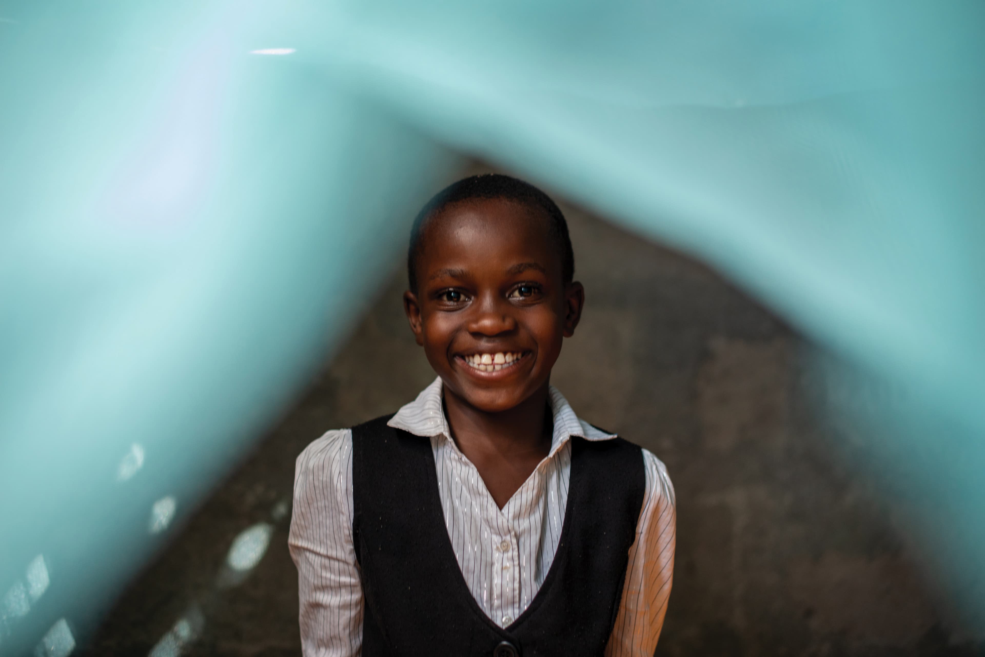 Girl wearing black vest and striped white shirt smiles, standing underneath a mosquito net.