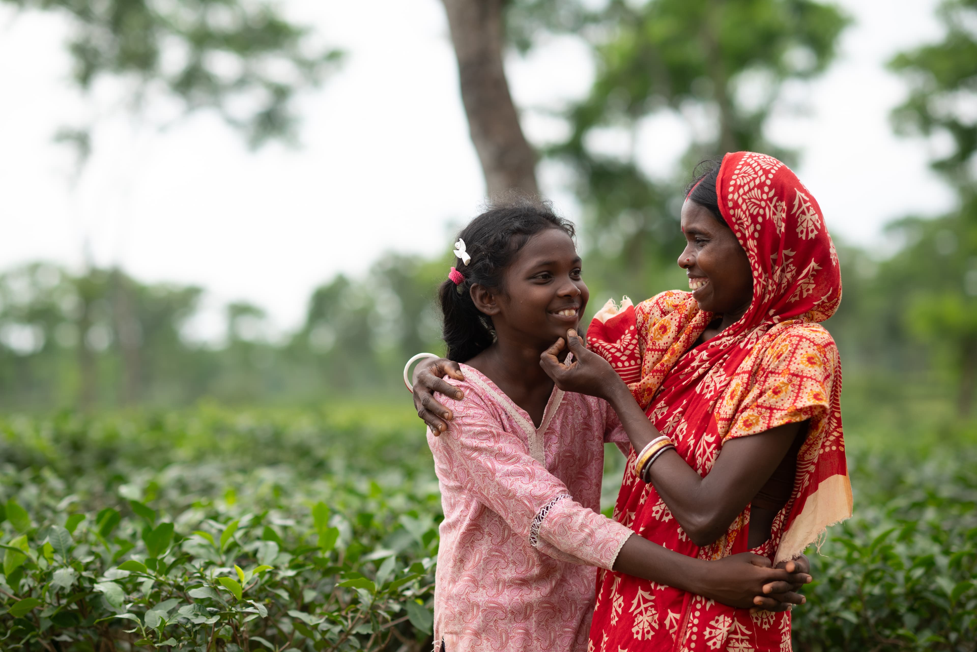 A mother and daughter are standing side-by-side in a tea field.