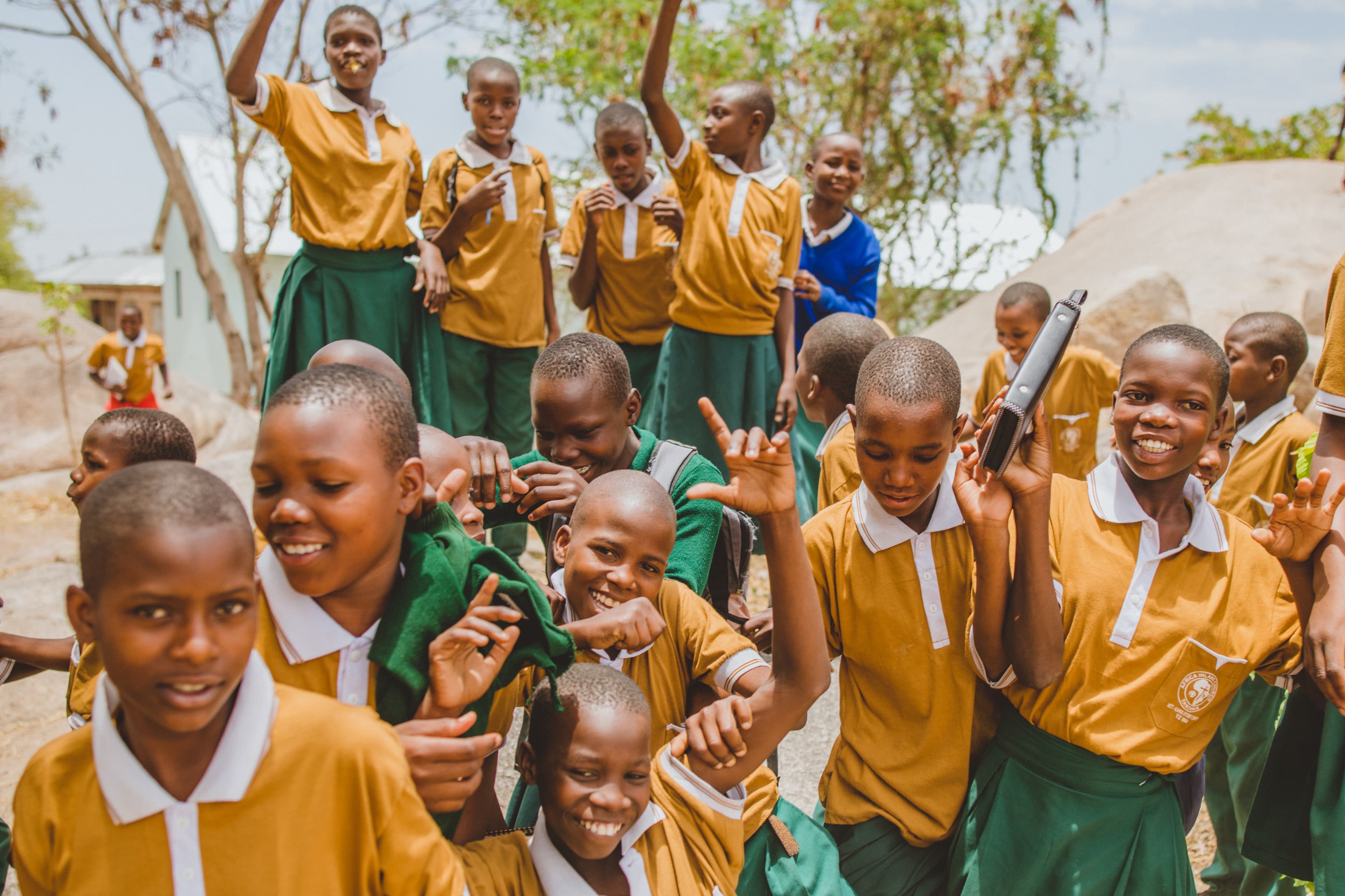 A group of African children wearing school uniforms laugh and smile.