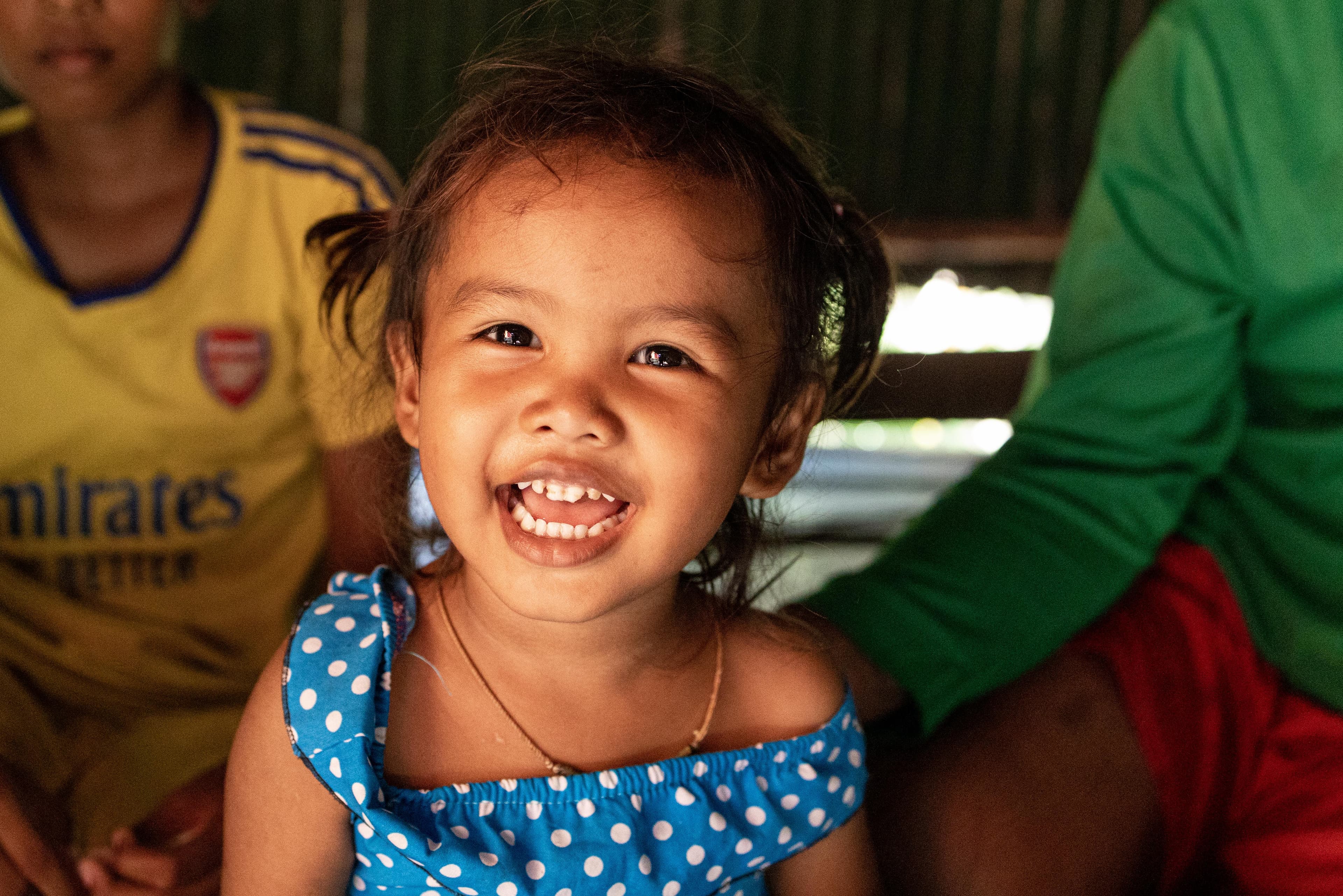 A young girl wearing a blue polka dot dress smiles for the camera.