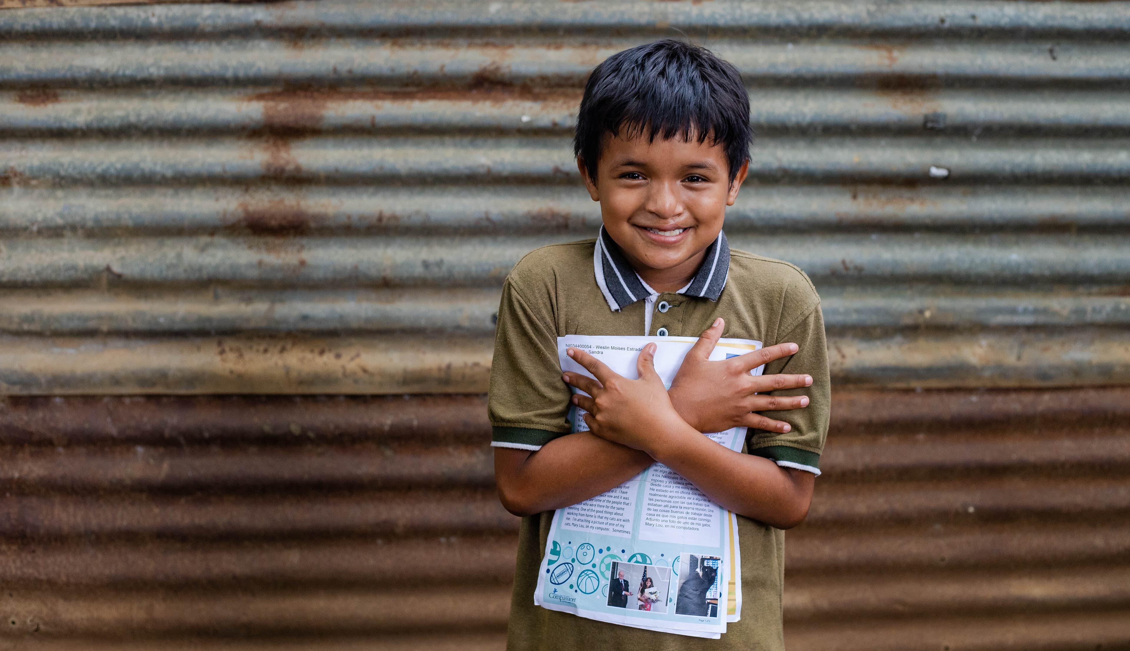 A young boy smiles as she holds tightly to a letter from his sponsor.