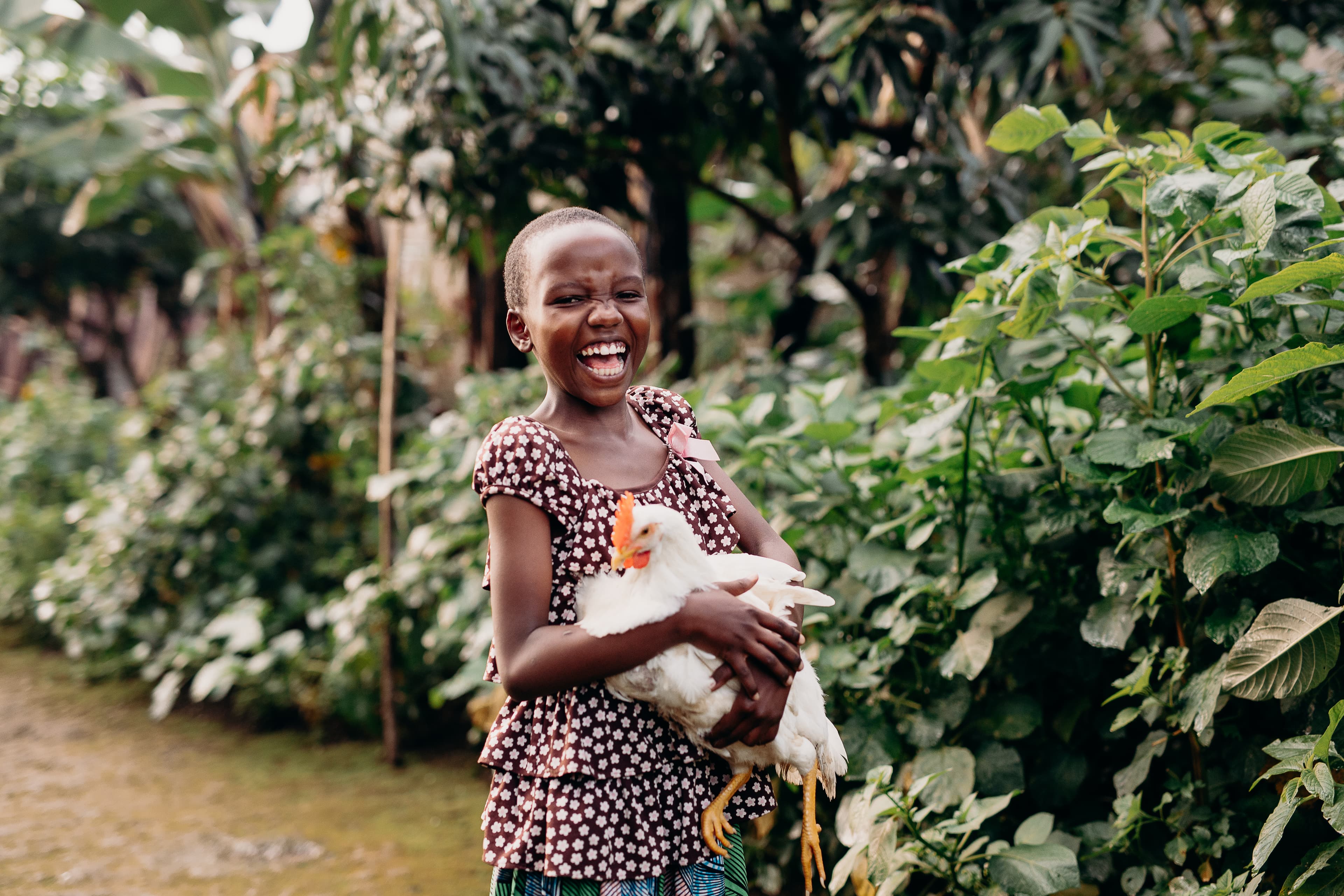 A young African girl holds a chicken while smiling brightly.