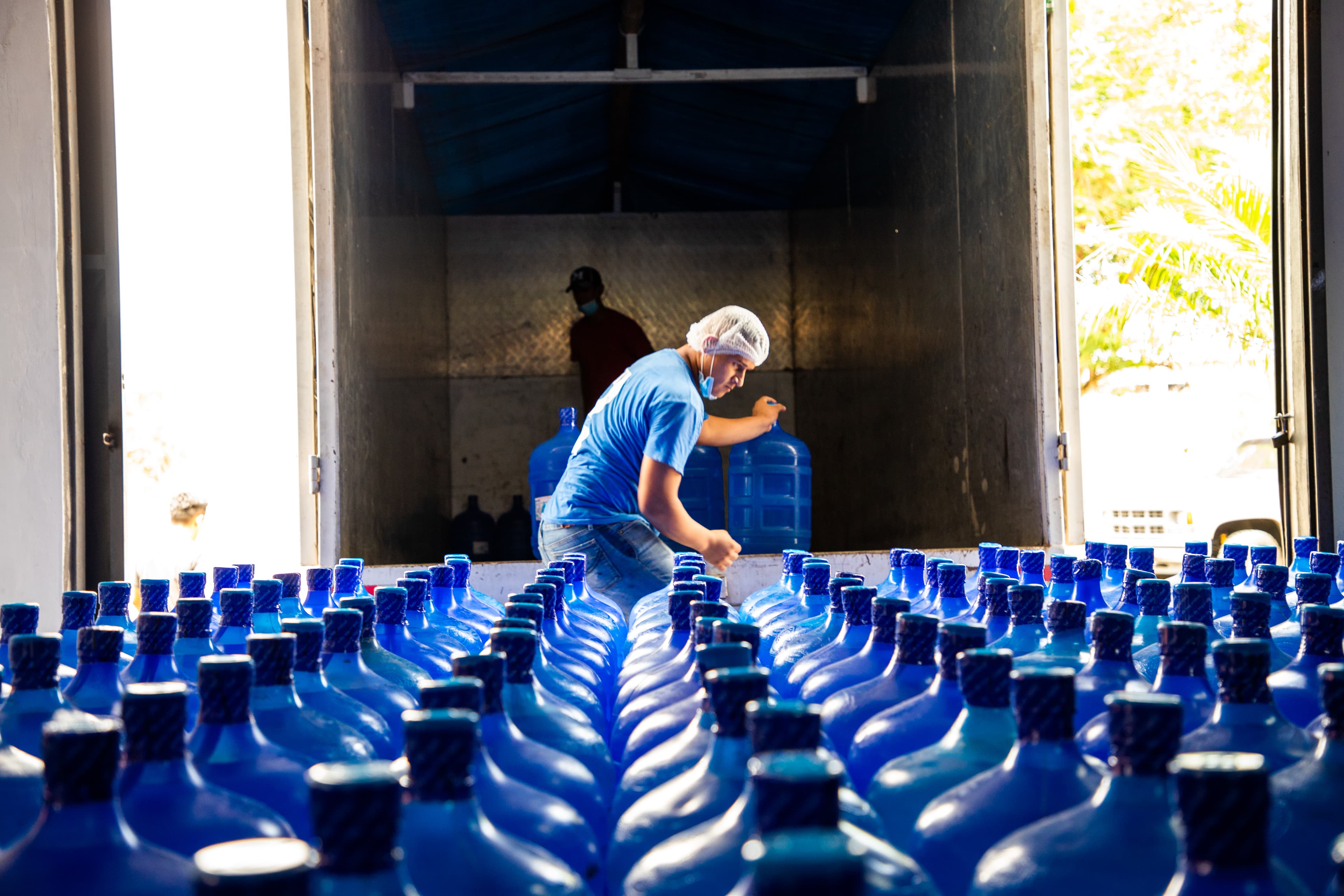 A young man loads blue water jugs onto a truck.