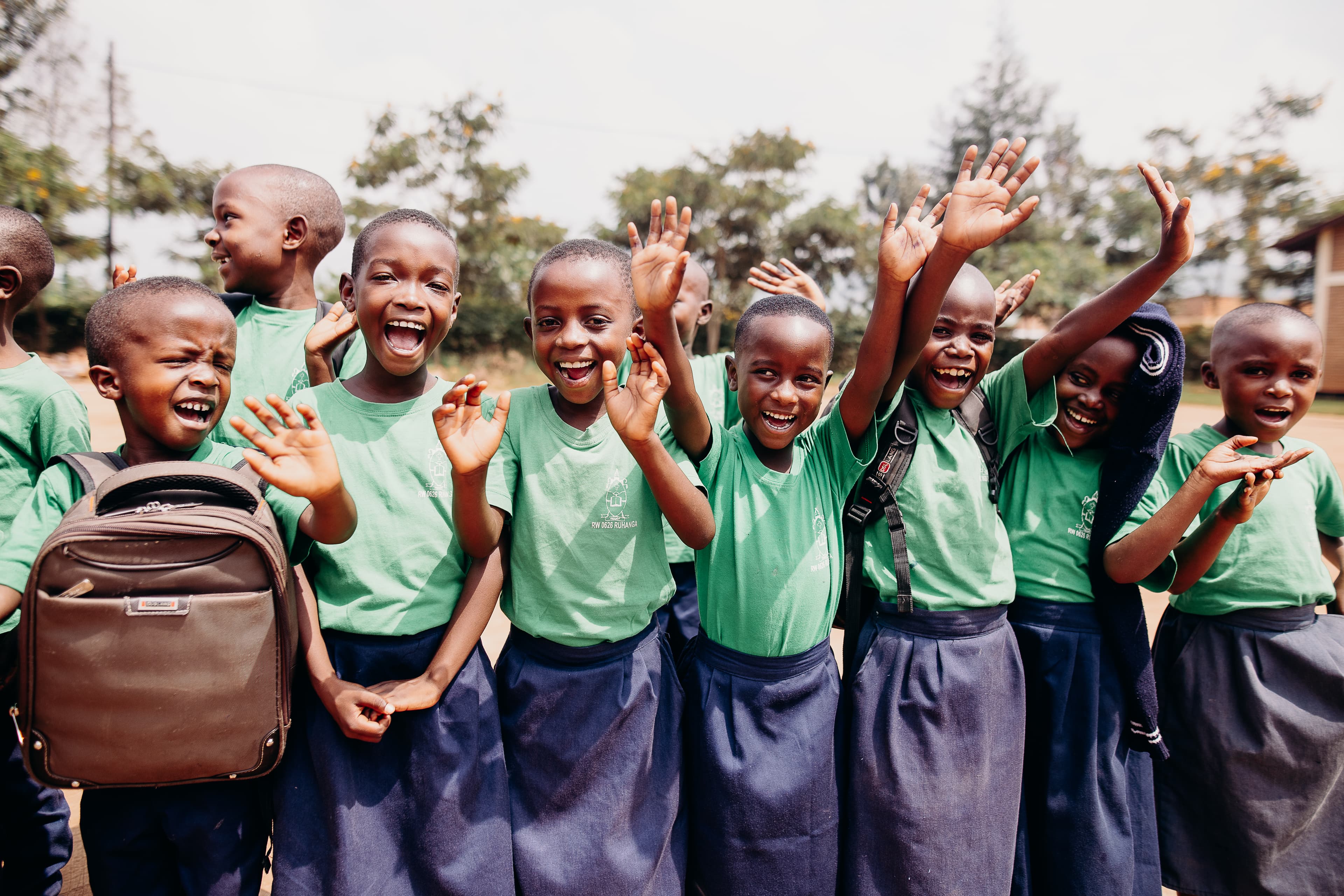 A group of African children wearing school uniforms wave and smile for the camera.