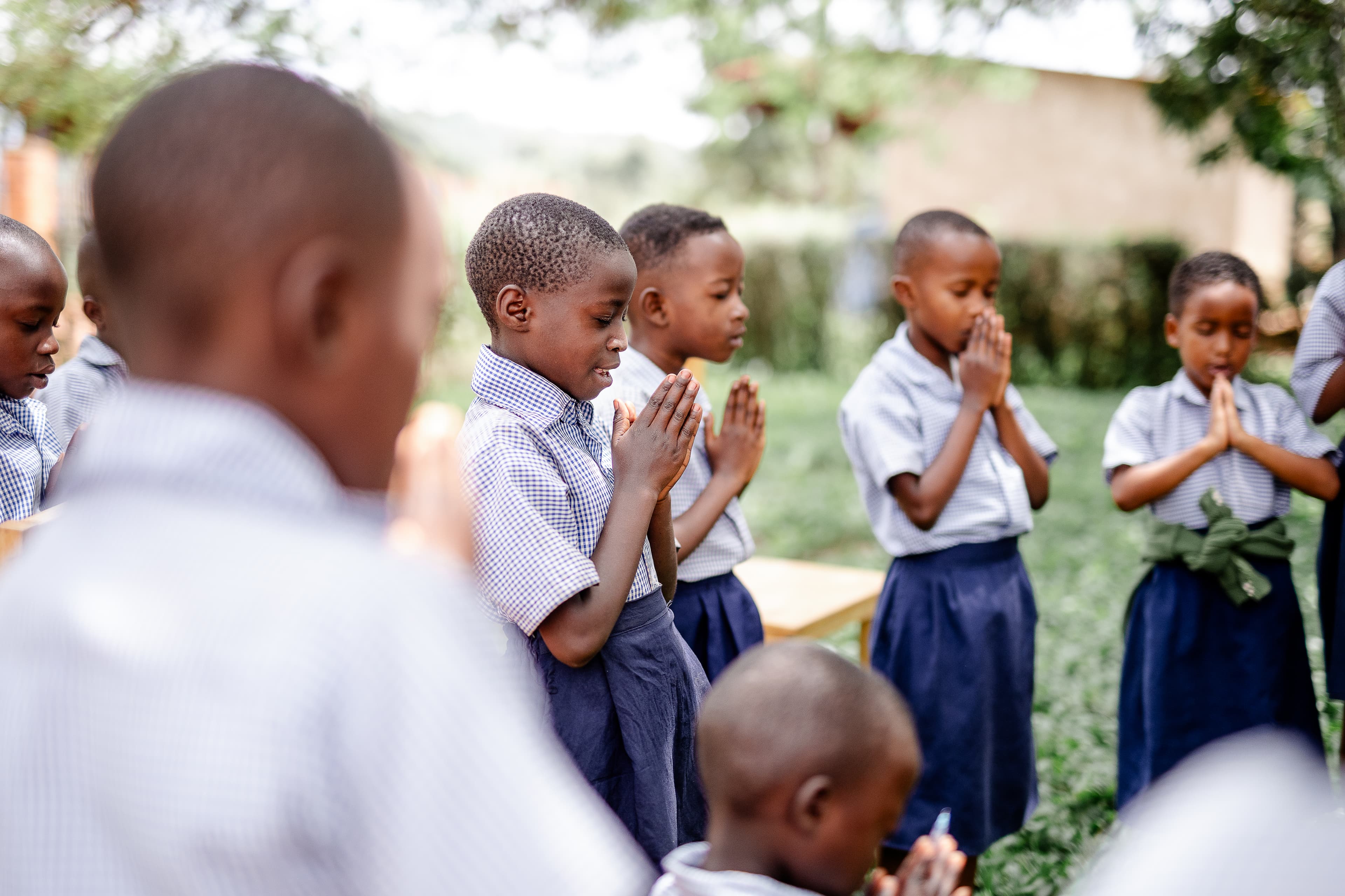 A group of students are standing together and praying surrounded by green trees