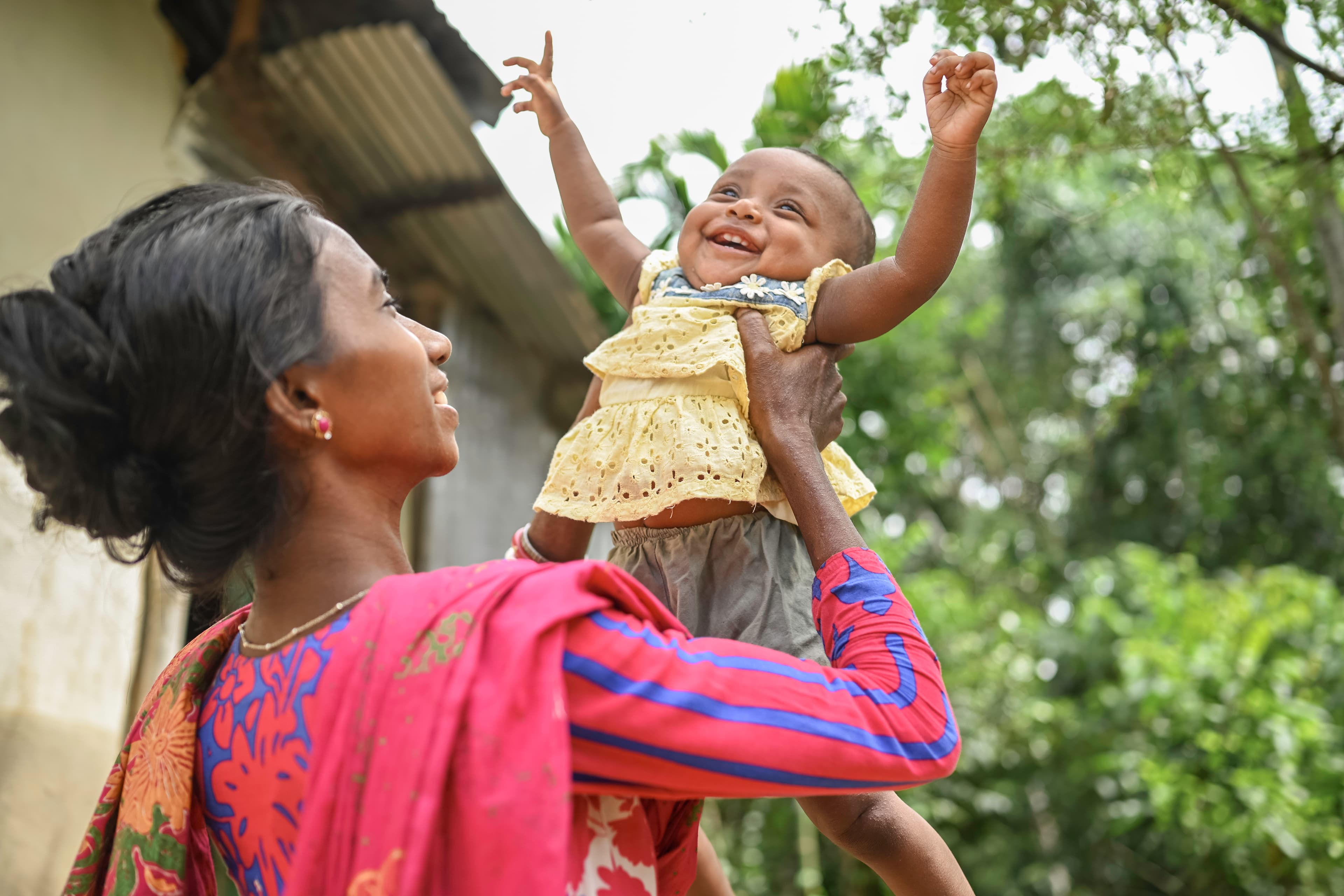 Woman is smiling as she lifts her daughter up in the air.