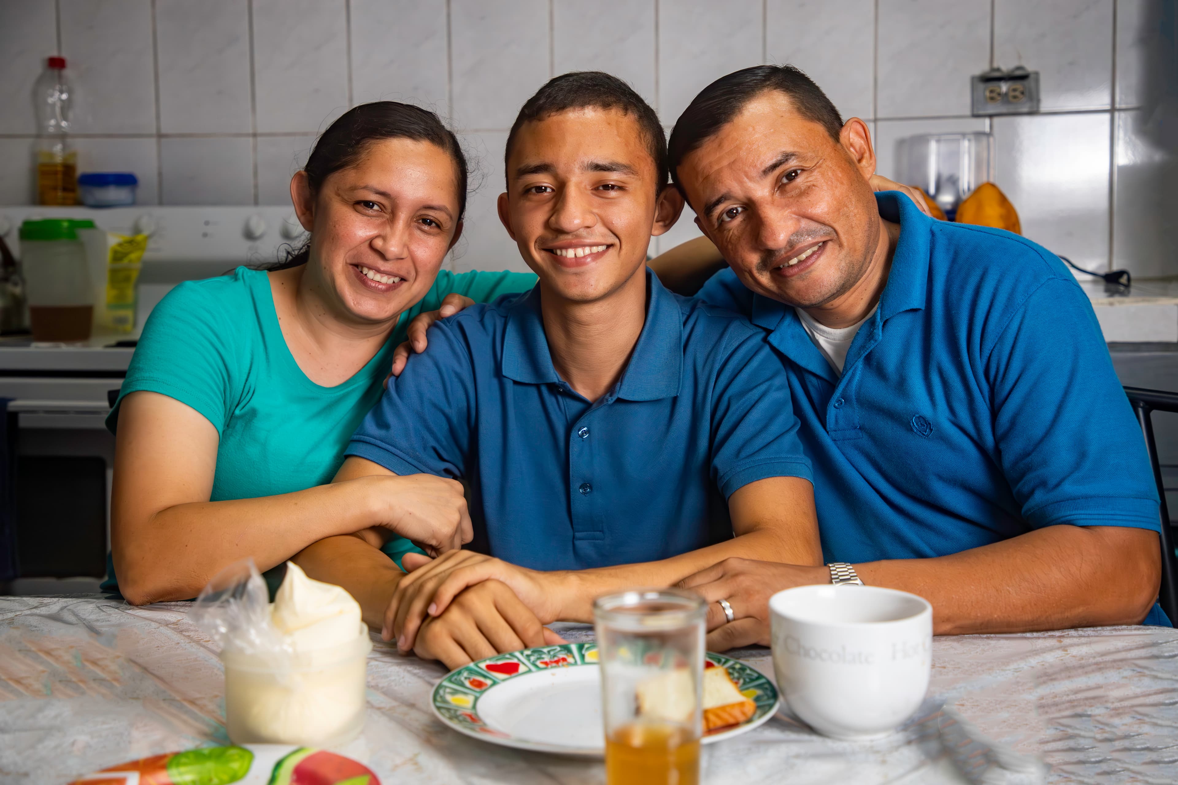 A teen boy sits between his mother and father as they all smile for the camera.