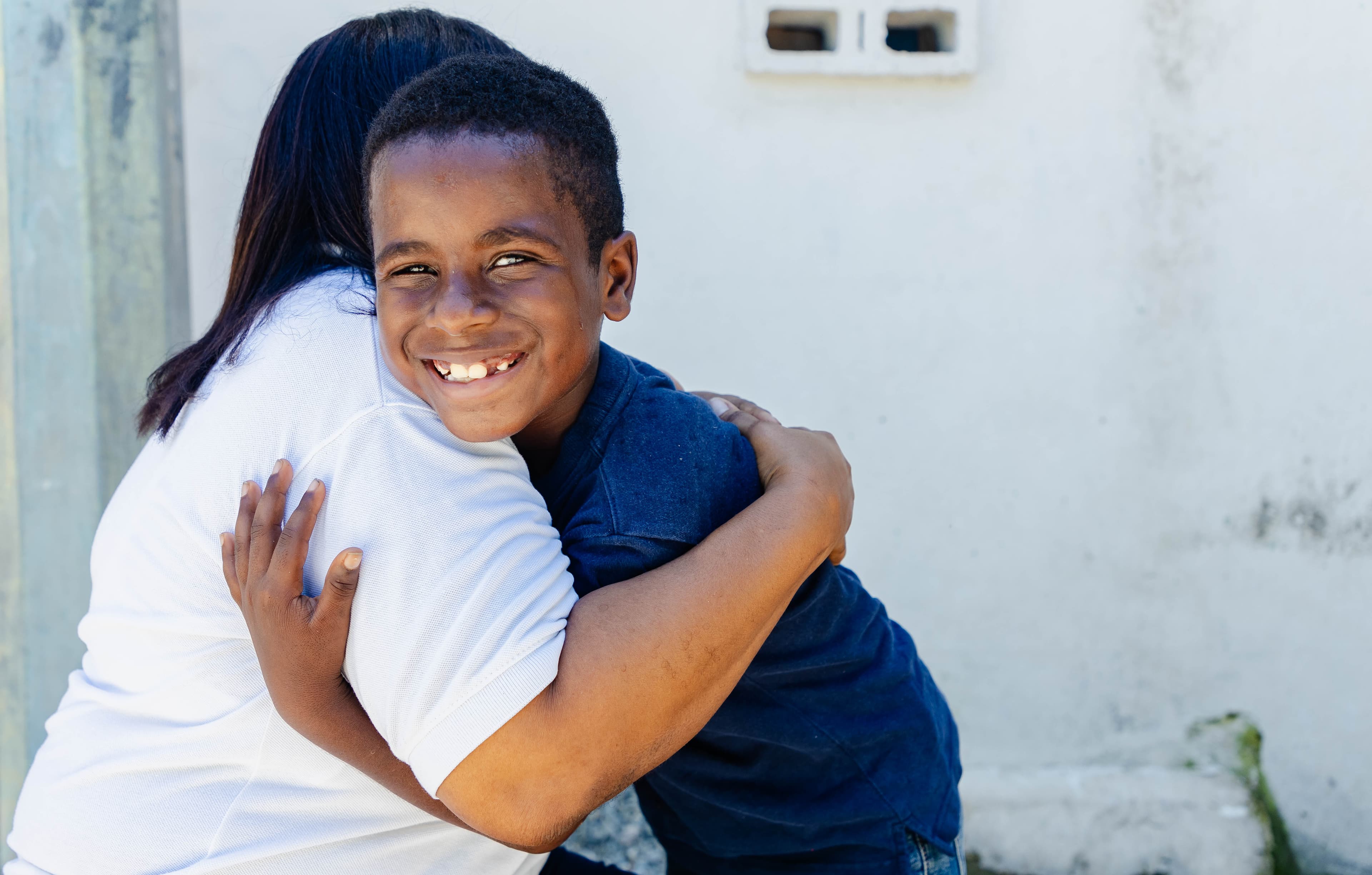 A young boy from the Dominican Republic hugs his mother while smiling for the camera.