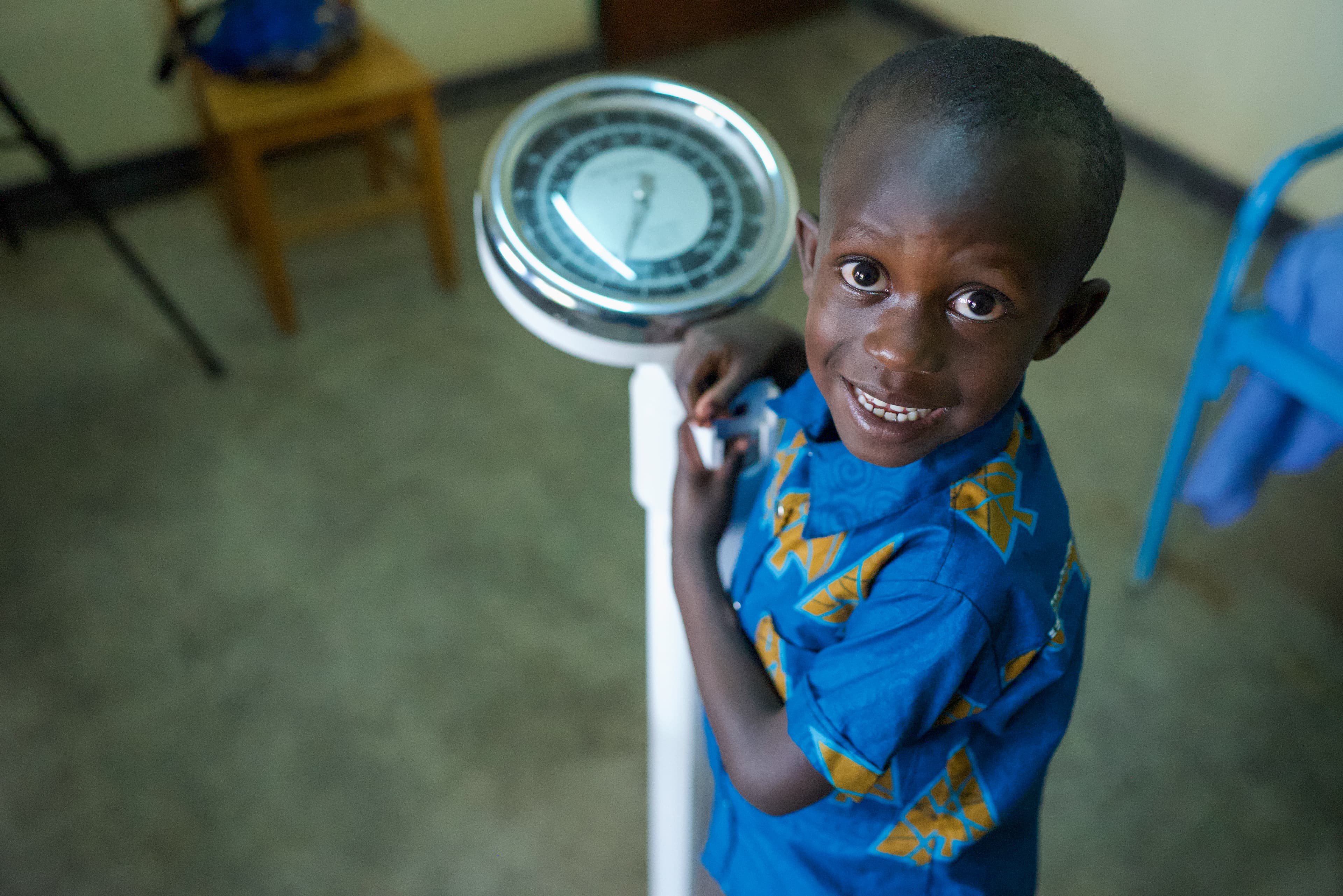 Young African boy stands on a scale while smiling for the camera.