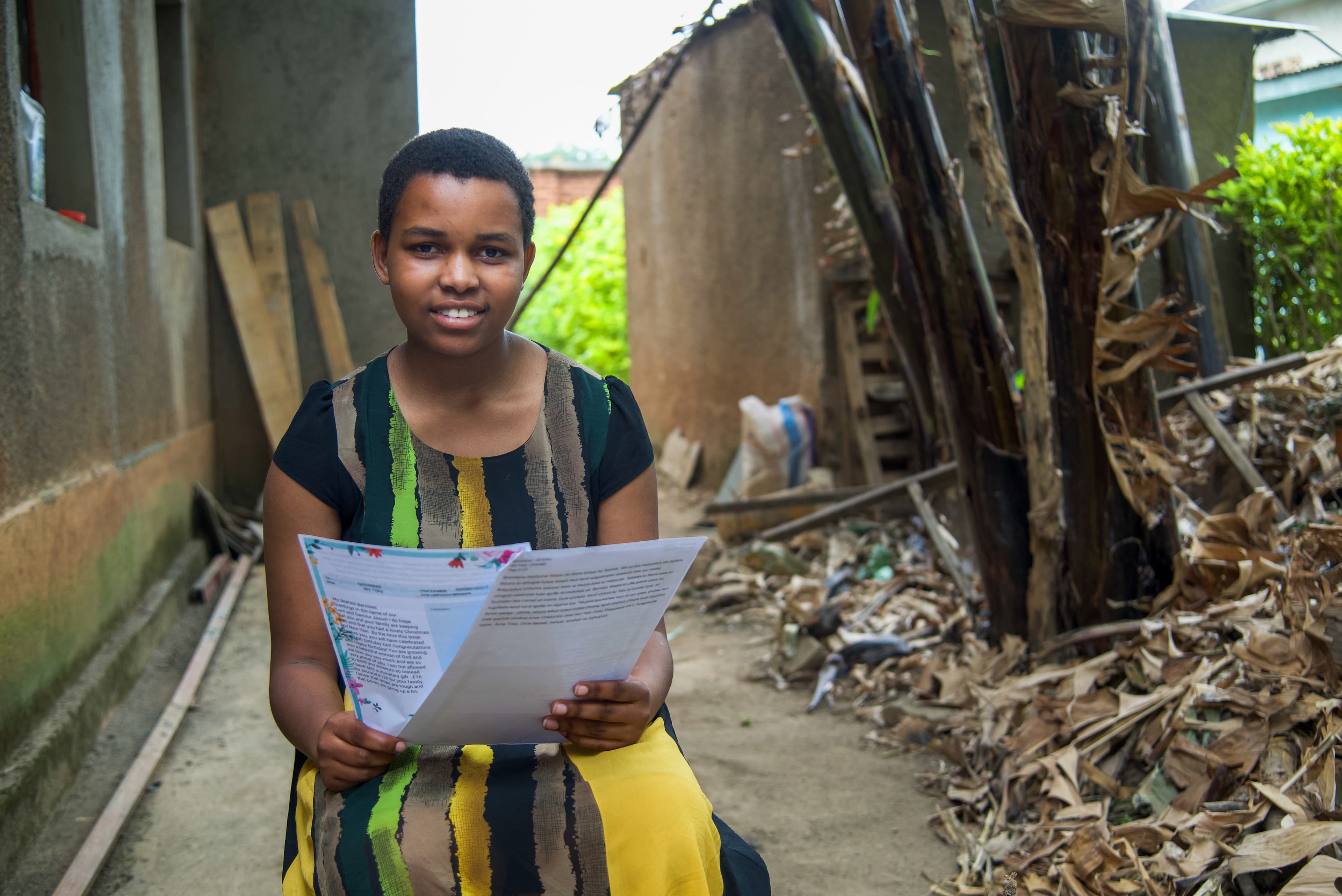 A teen African girl sits and holds letters while smiling.