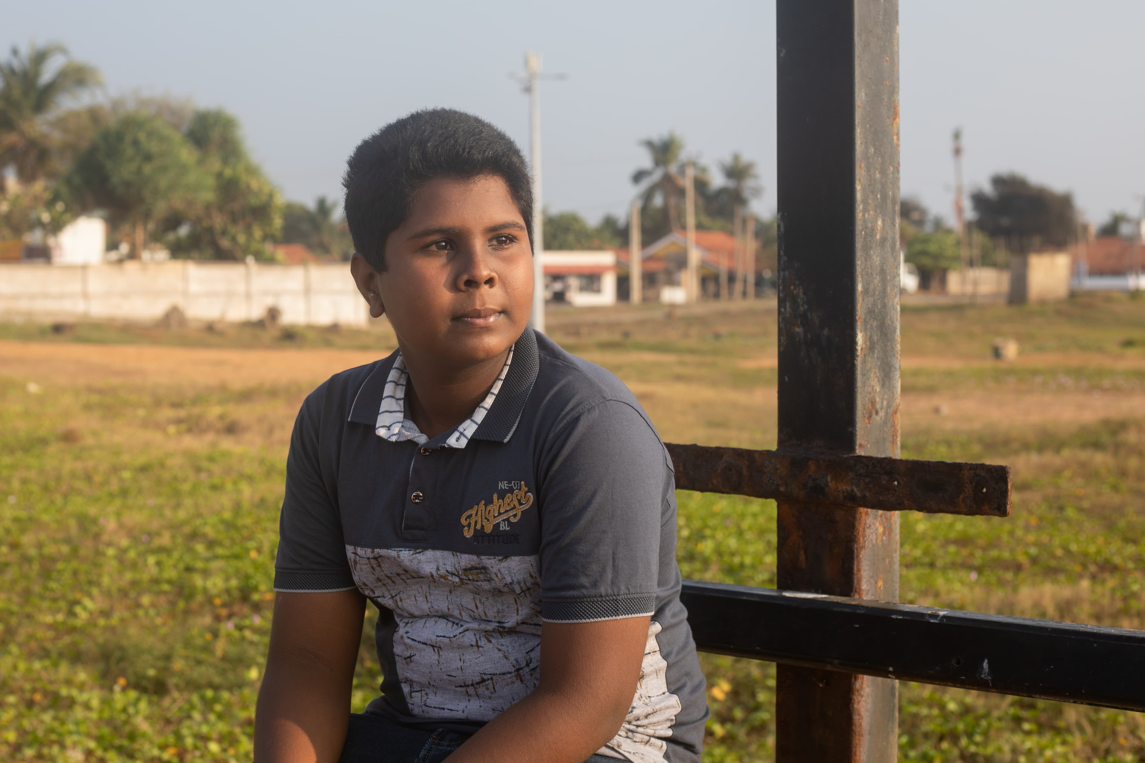A young boy is sitting on a bench looking out in the distance.