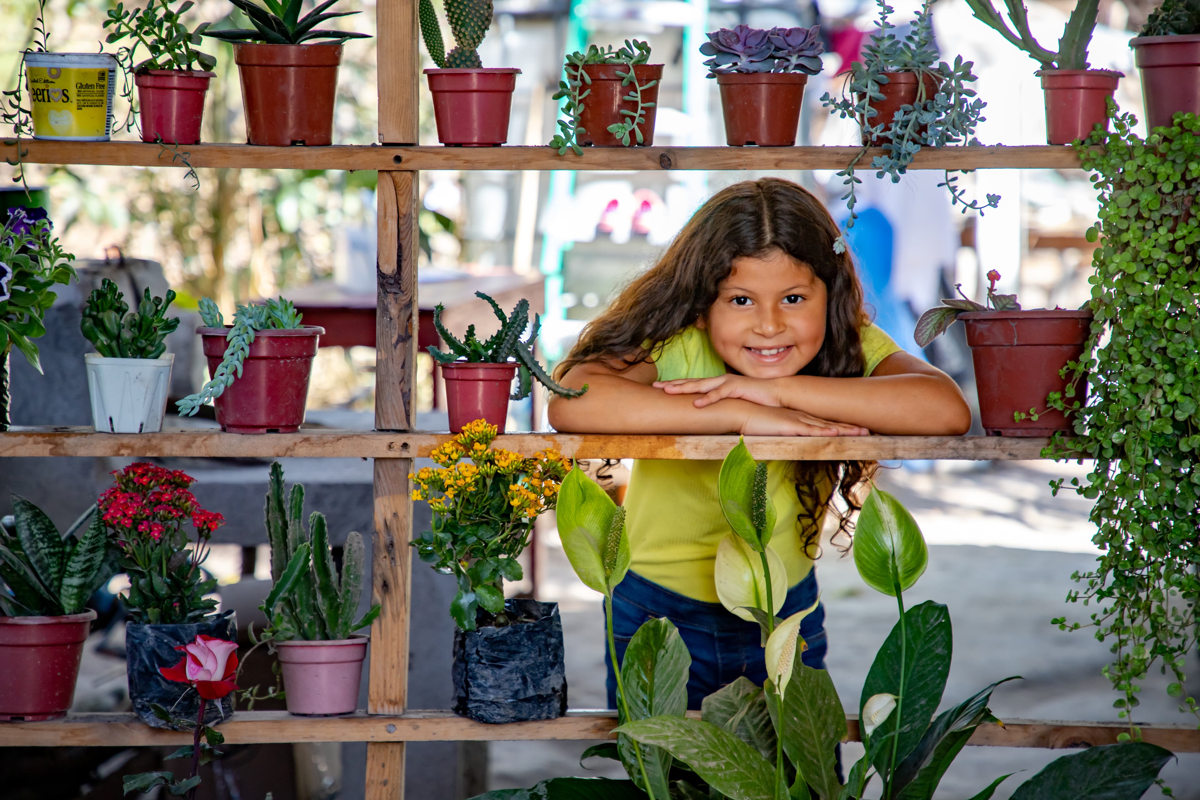 A young girl is posing for a photo with the ornamental plants her mother sells for a living.