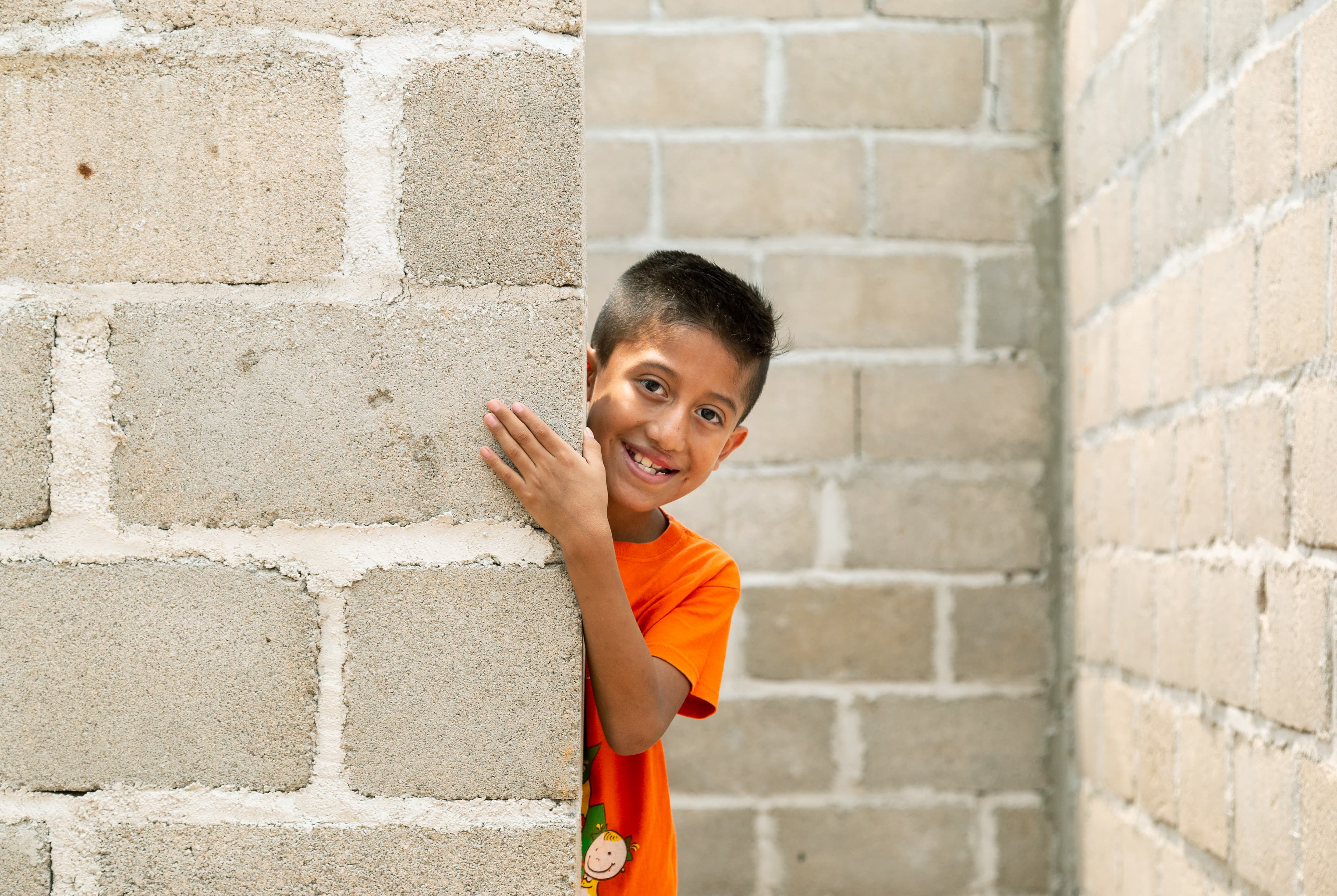 A young boy is playfully hiding behind a wall under construction at their new home.