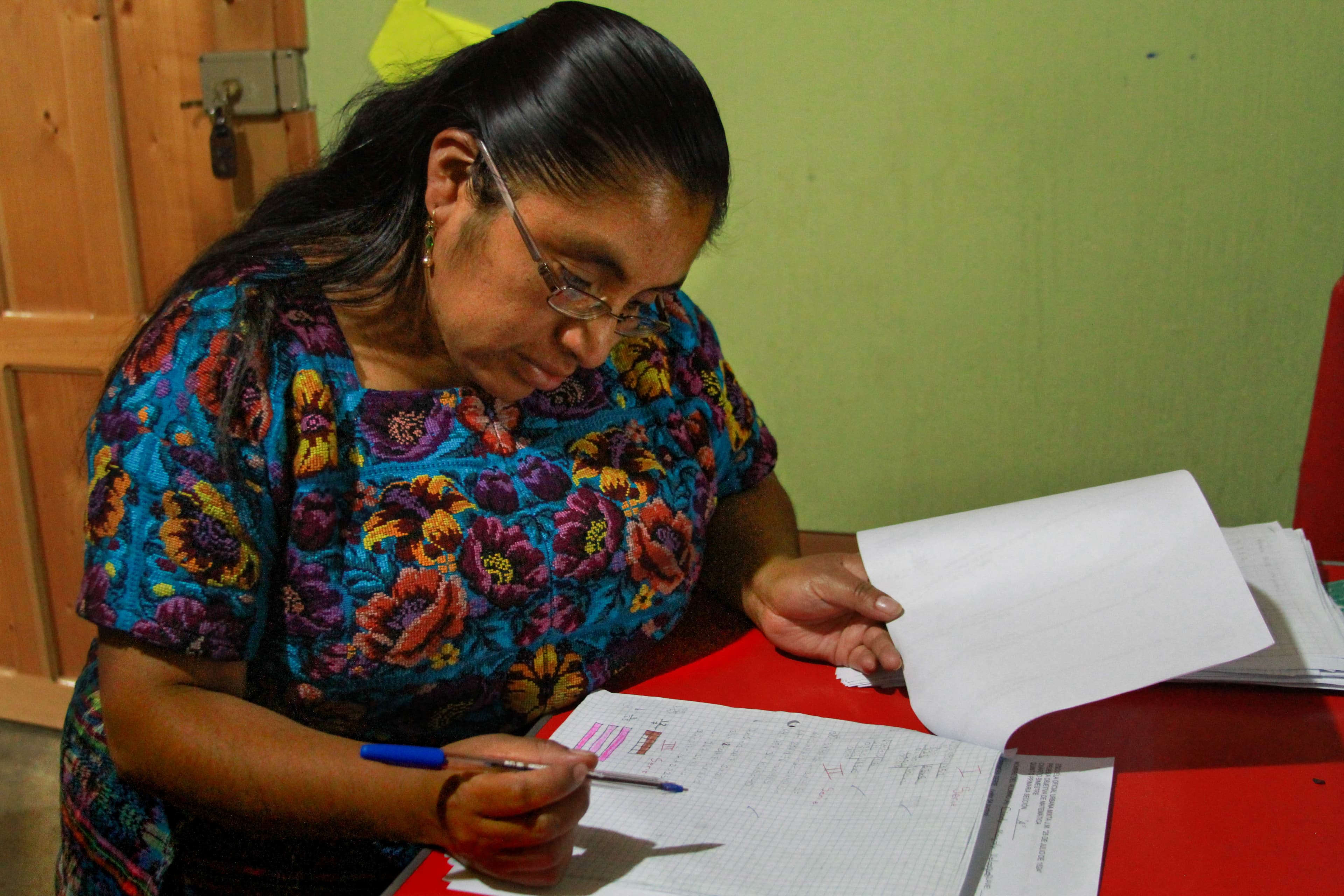 Bianca is sitting at a desk reading a paper with a pen in her hand.