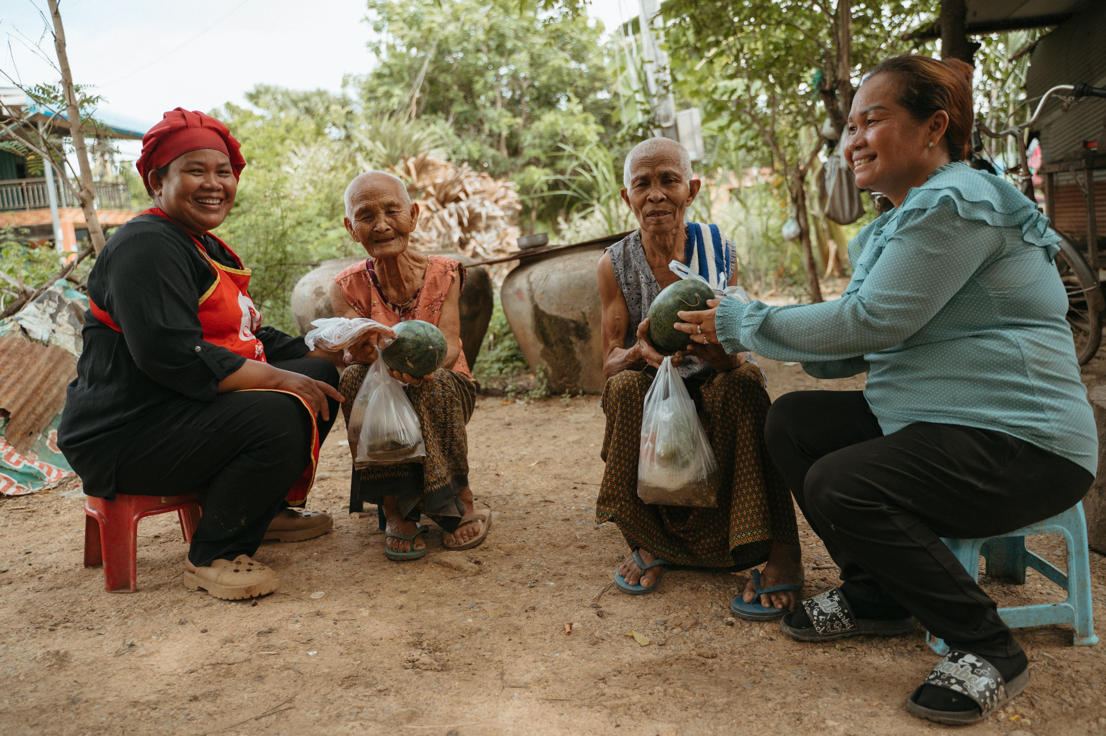 Two older women give fruit to two other women while they smile for the camera.