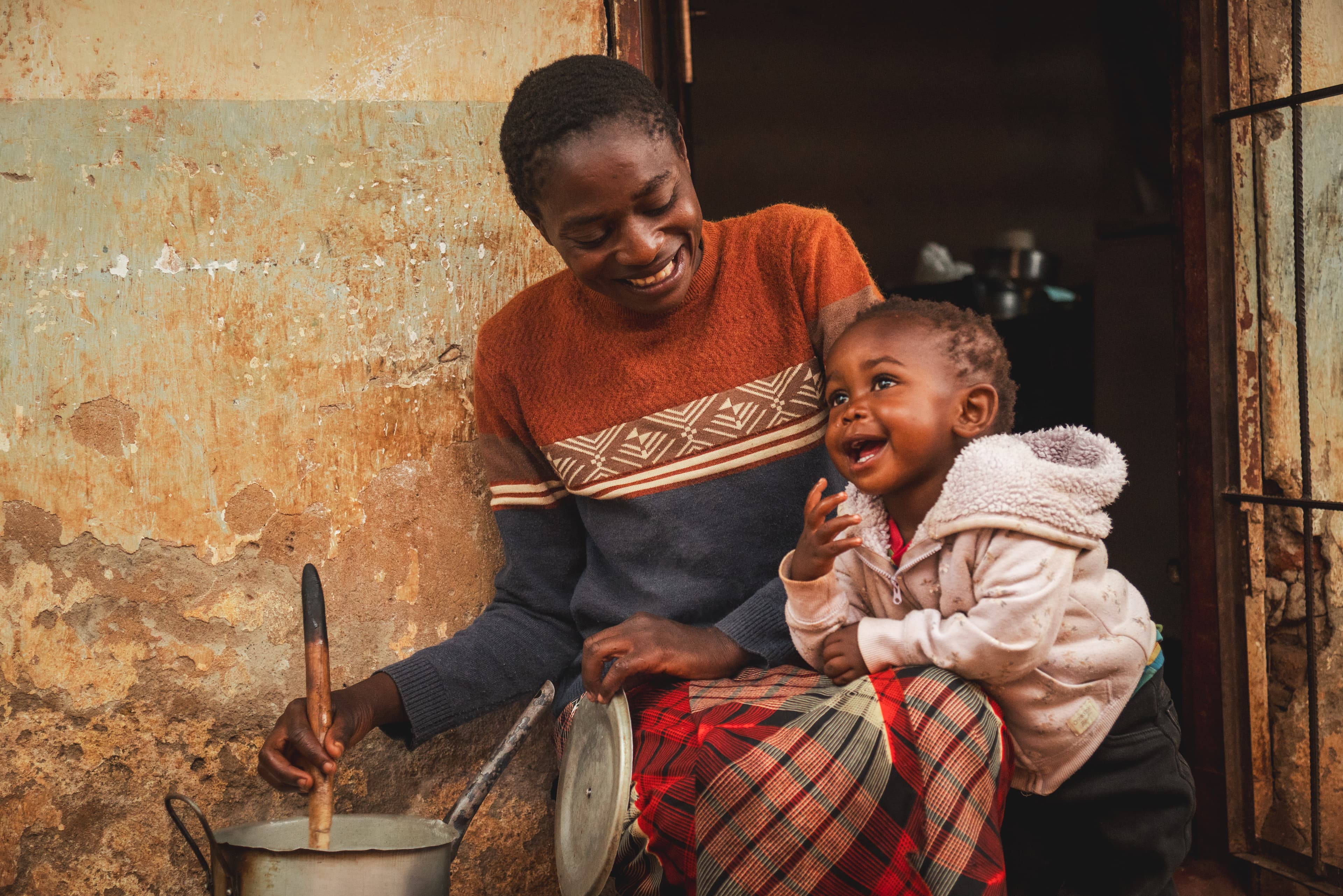 An African mom smiles at her toddler daughter as they sit outside of their home.
