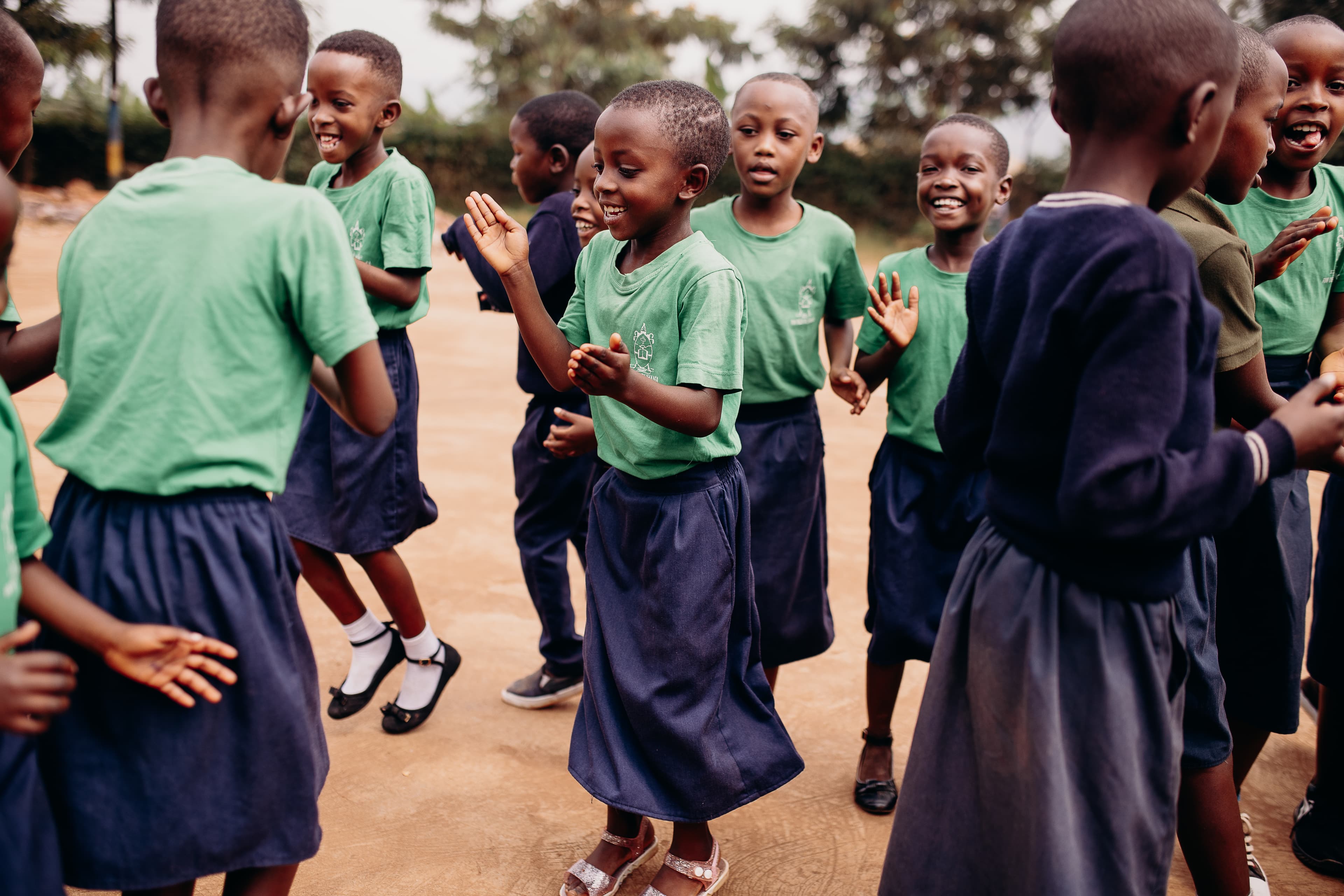 A group of children in school uniforms are dancing and clapping outside.